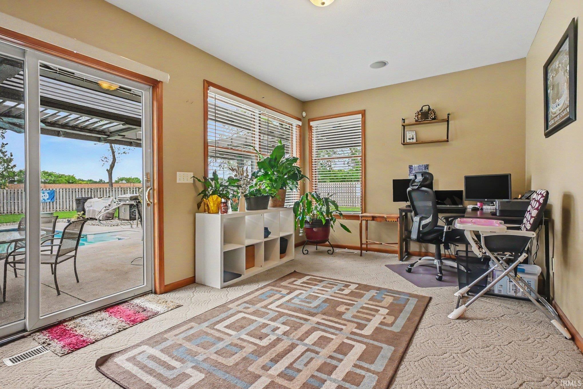 Carpeted interior space featuring a sliding glass door providing access to a concrete patio with an outdoor pool
