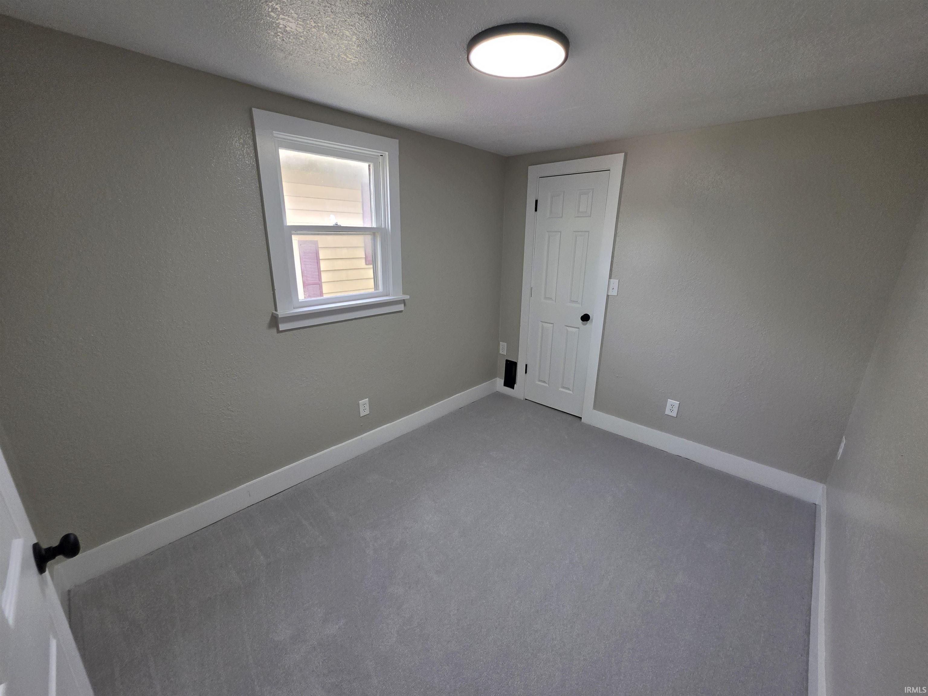 Neutral-toned room featuring light gray carpet flooring, white baseboards, and a white paneled door with matte black hardware