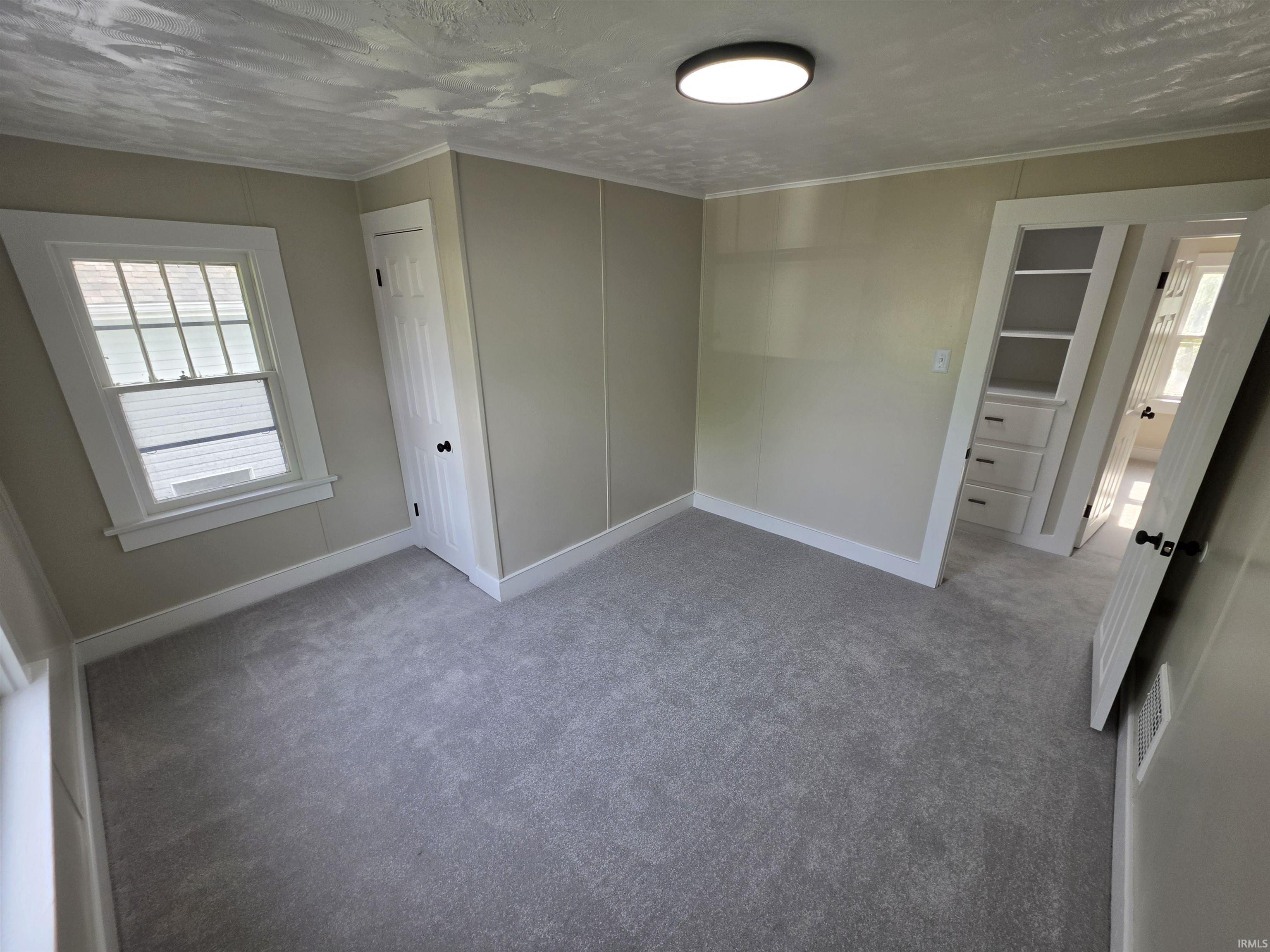 Carpeted room featuring a double-hung window, built-in shelving, built-in drawers, and a ceiling-mounted light fixture