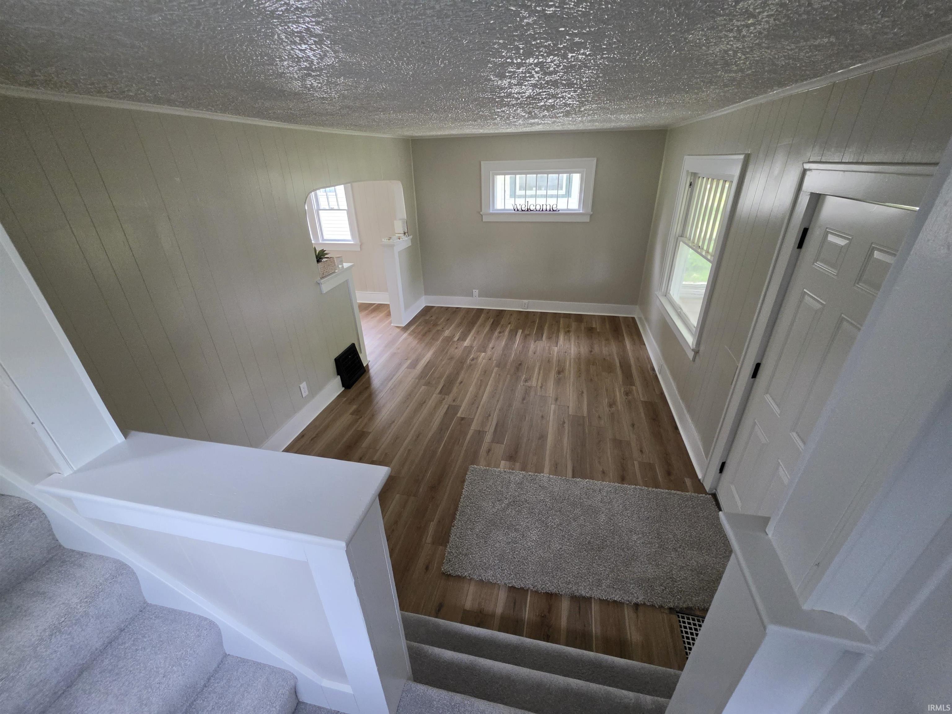 Open concept living area featuring wood-finish flooring, light-toned wall paneling, and white trim