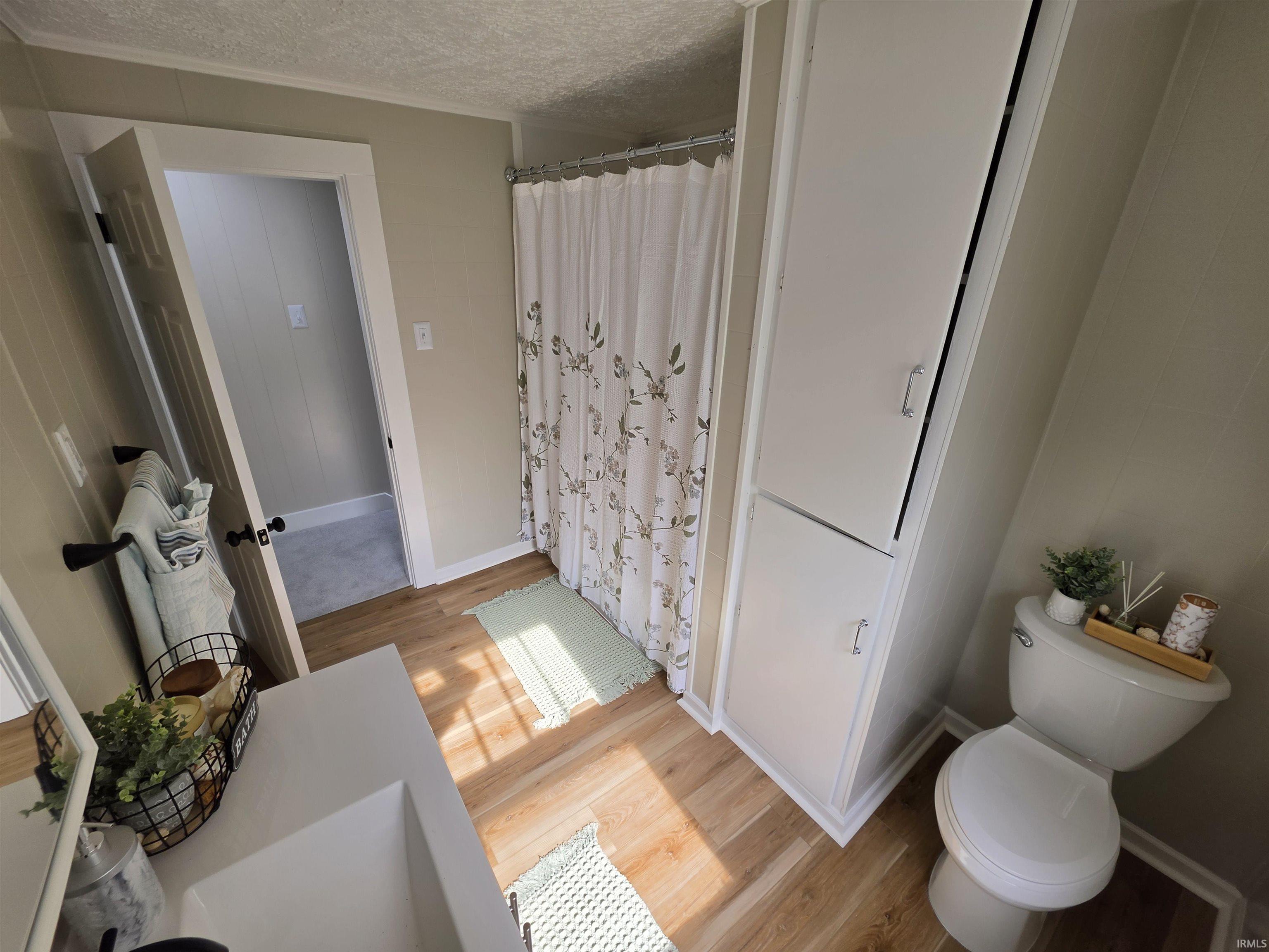 Bathroom featuring wood-finish flooring, built-in vertical cabinetry, a white toilet, a shower with a curtain, and a vanity with an integrated white sink