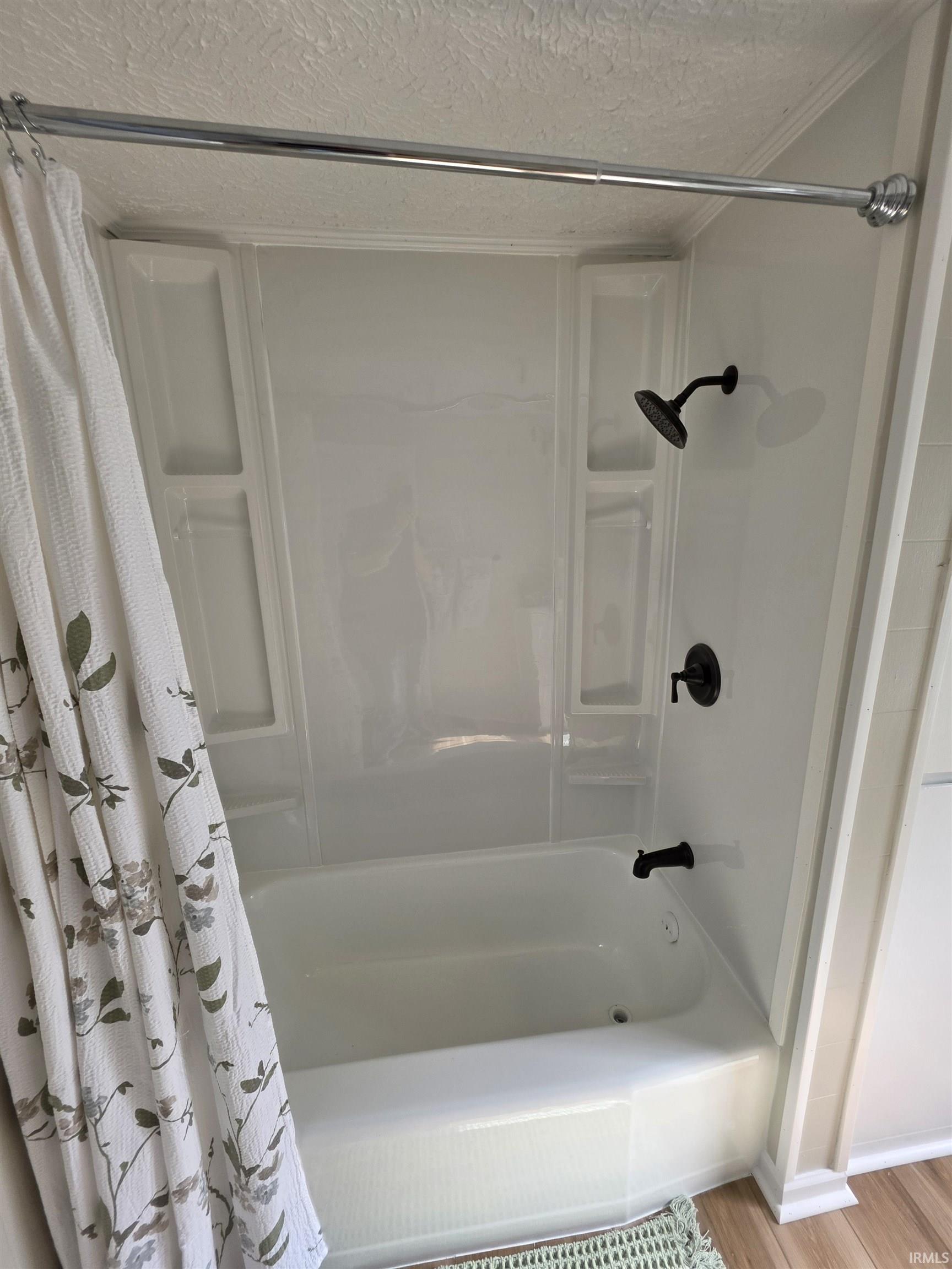 White acrylic tub and shower combination with integrated shelving, matte black fixtures, and a chrome shower rod