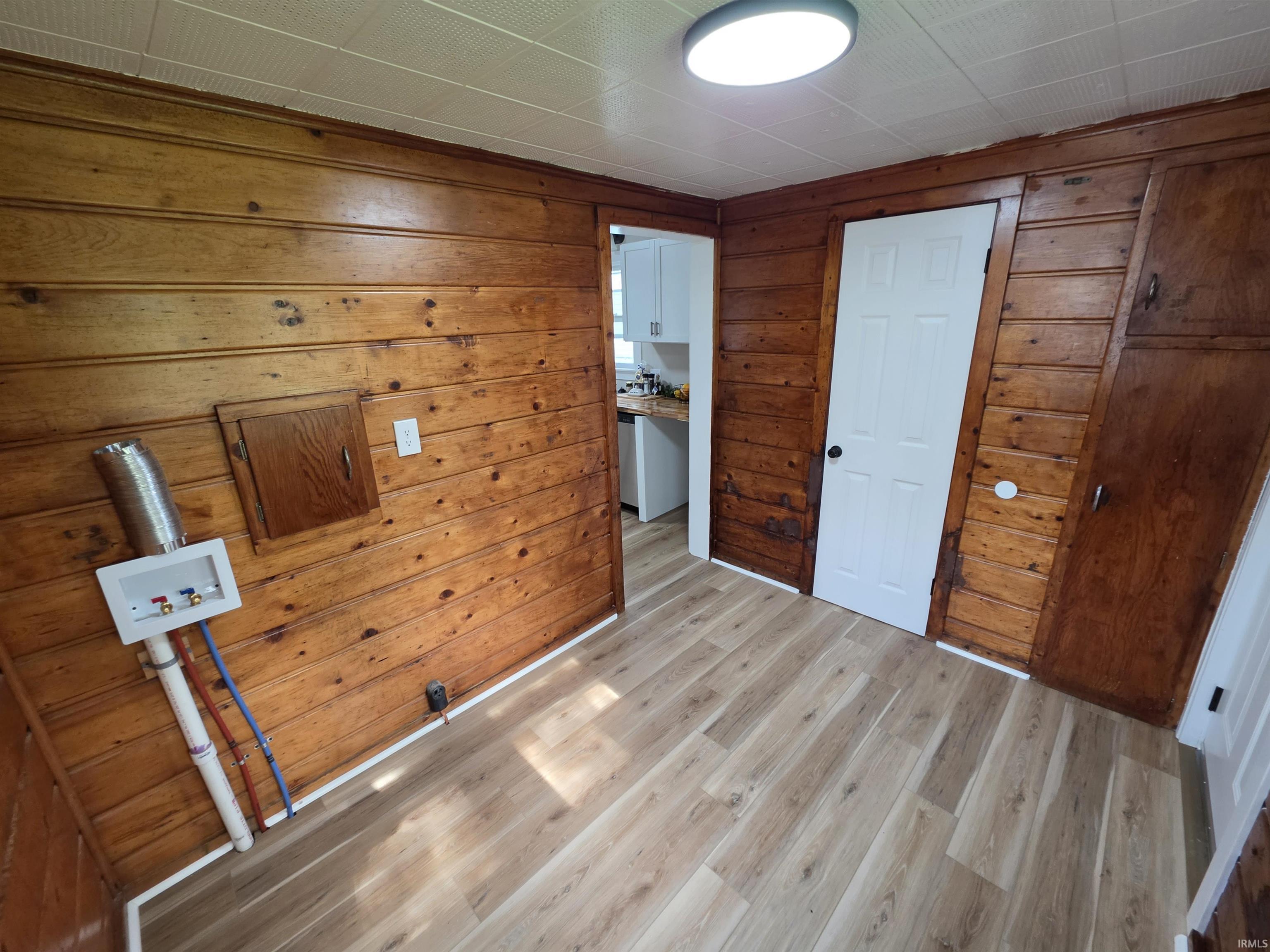 Laundry area featuring wood-finish flooring, wood paneling, utility hookups, a flush-mount ceiling light, and a built-in wood cabinet