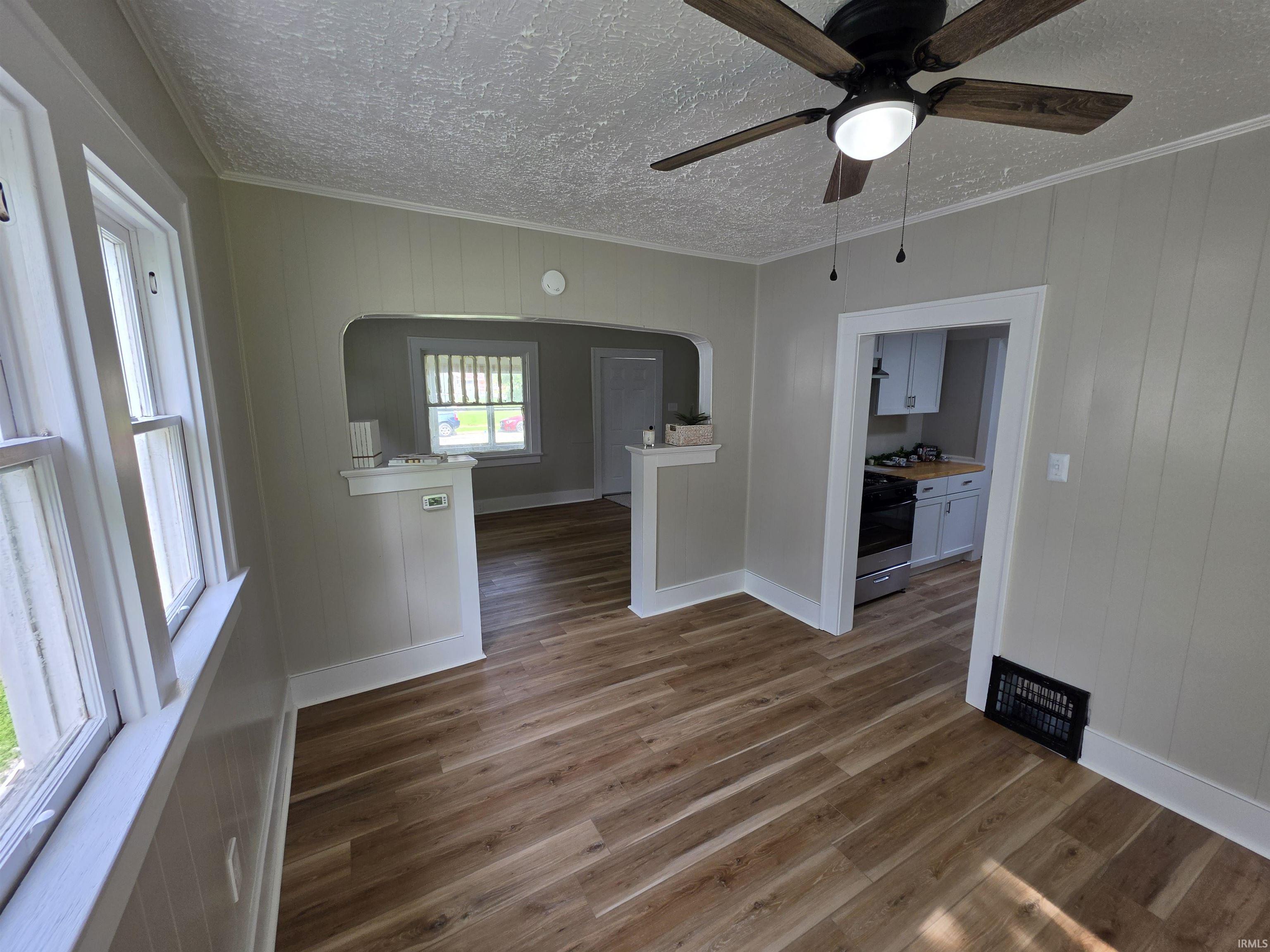 Open concept living space featuring wood-finish flooring, a ceiling fan with integrated lighting, and multiple windows