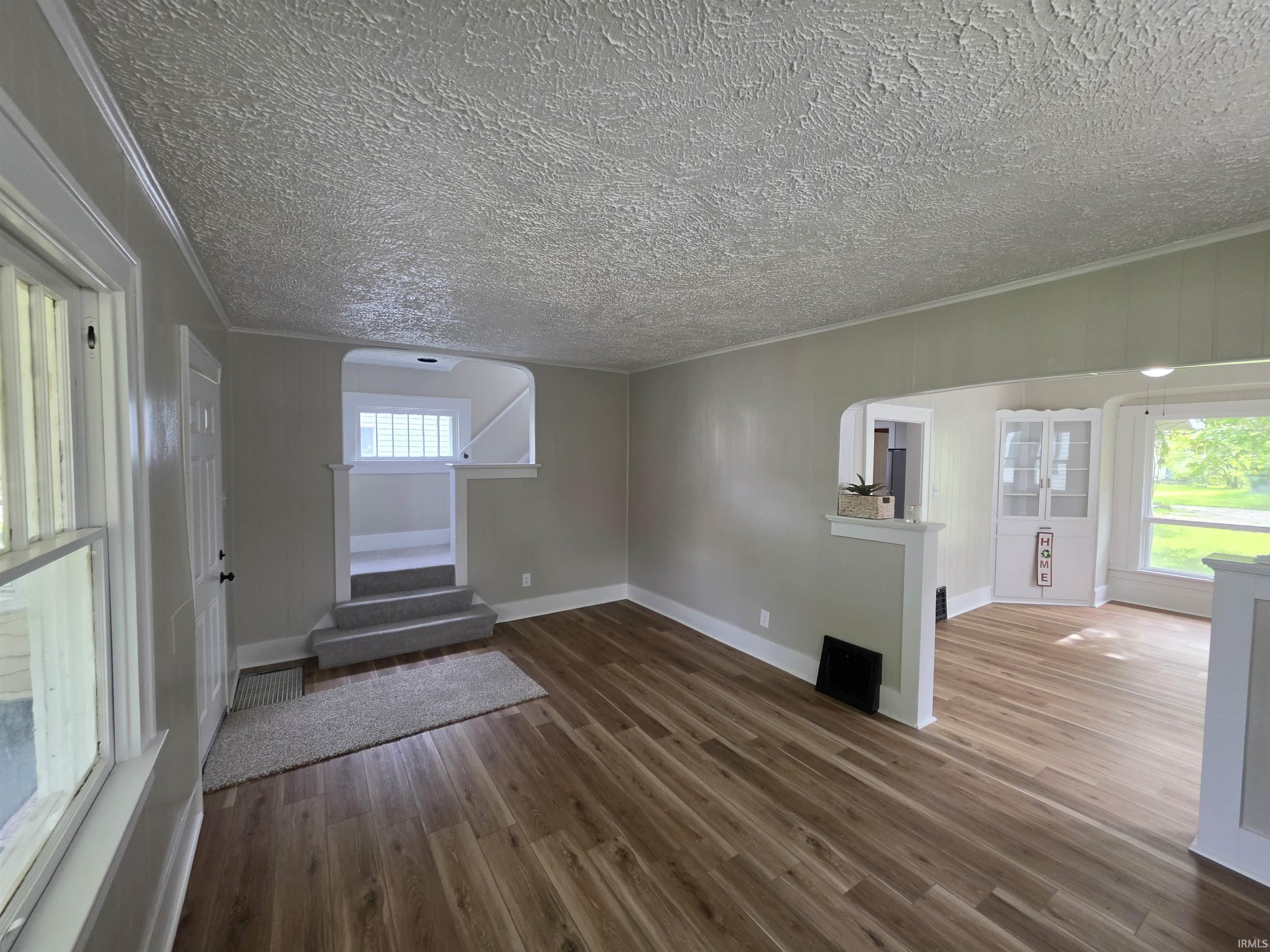 Spacious interior featuring wood-finish flooring, light grey wall paint, white trim, and a textured ceiling