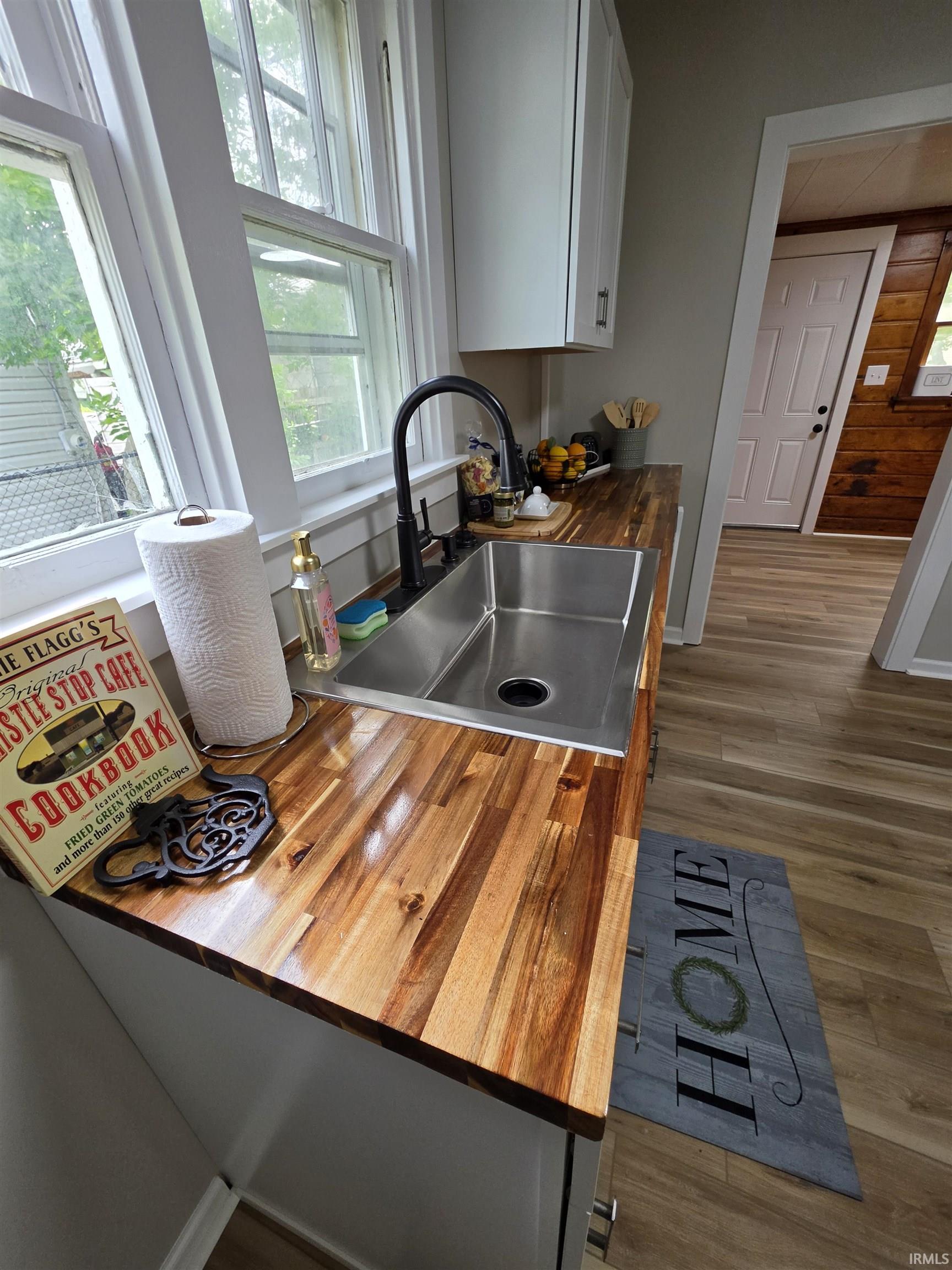 Kitchen area featuring a stainless steel undermount sink with a matte black faucet, warm wood-finish countertops, white shaker-style cabinetry, and wood-finish flooring