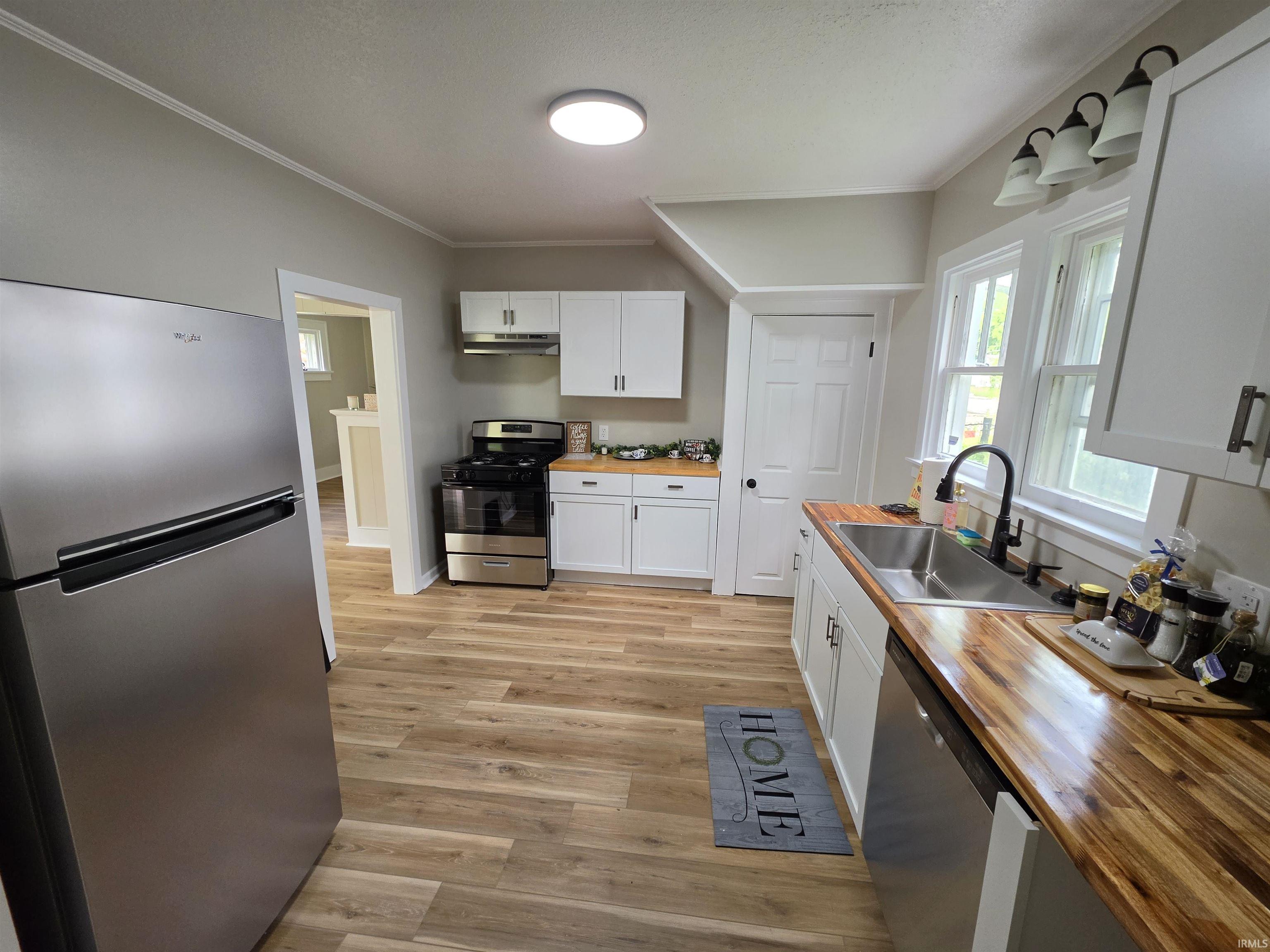 Kitchen featuring wood-finish flooring, white cabinetry with dark hardware, stainless steel appliances, and butcher block countertops