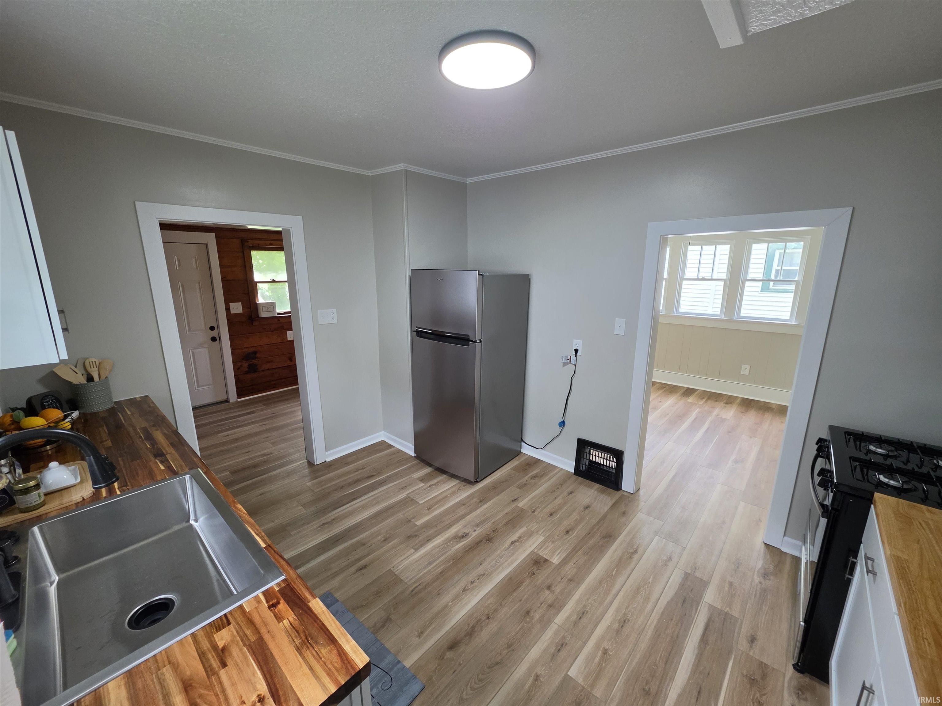 Kitchen featuring wood-finish flooring, butcher block countertops, an undermount stainless steel sink, and a stainless steel refrigerator