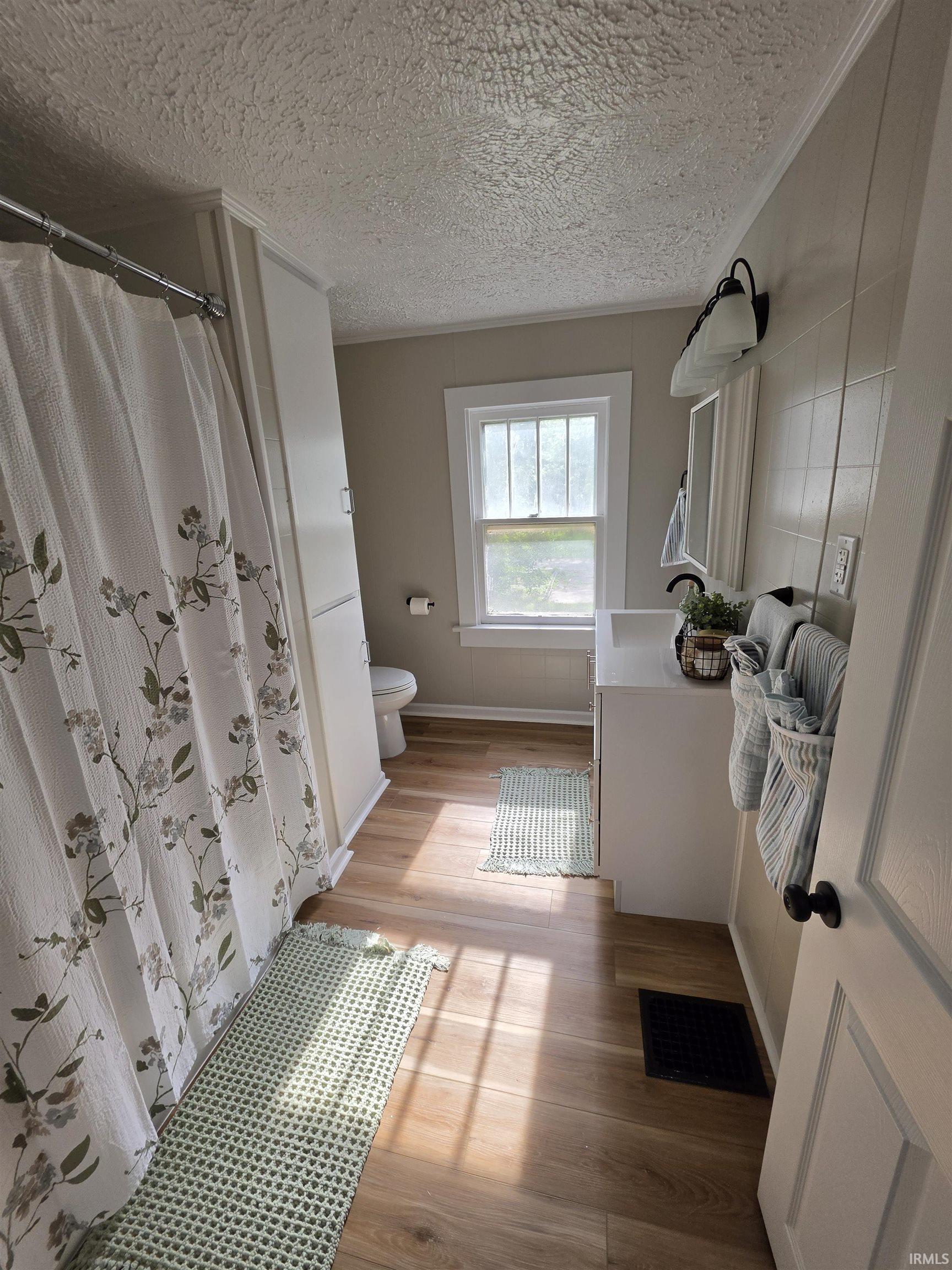 Bathroom with wood-finish flooring, a single window, white vanity, built-in storage cabinetry, and wall-mounted light fixture