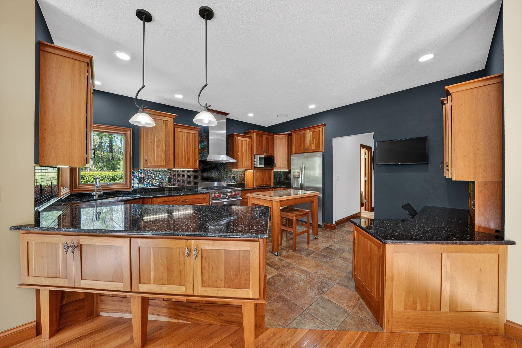 Custom wood cabinetry with dark countertops and modern pendant lighting