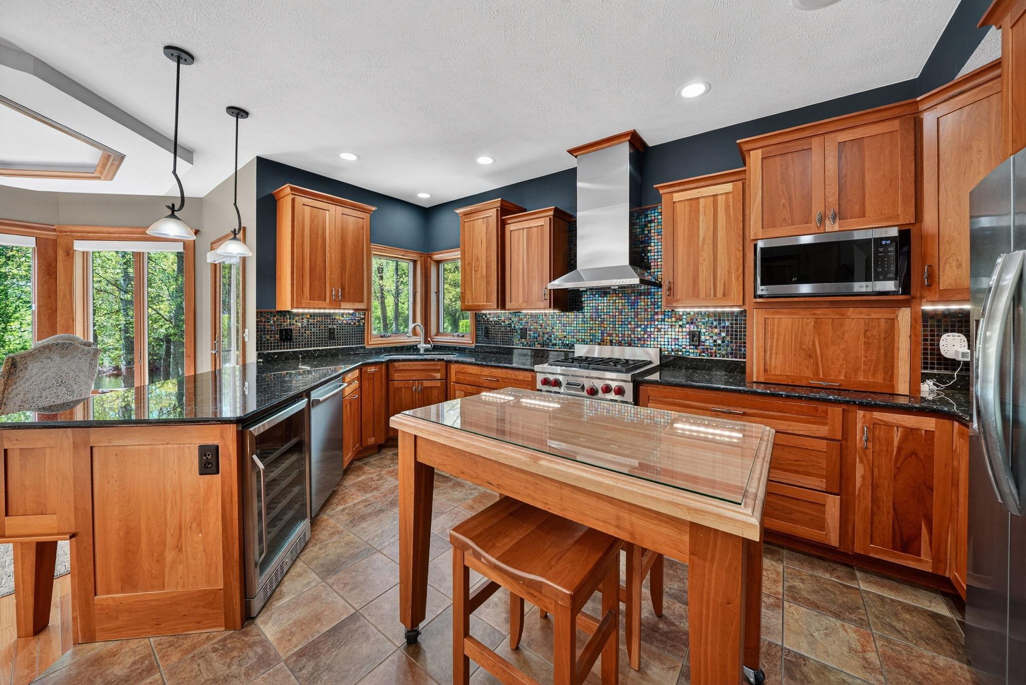 Spacious kitchen featuring warm wood cabinetry, dark granite countertops, and a vibrant mosaic tile backsplash