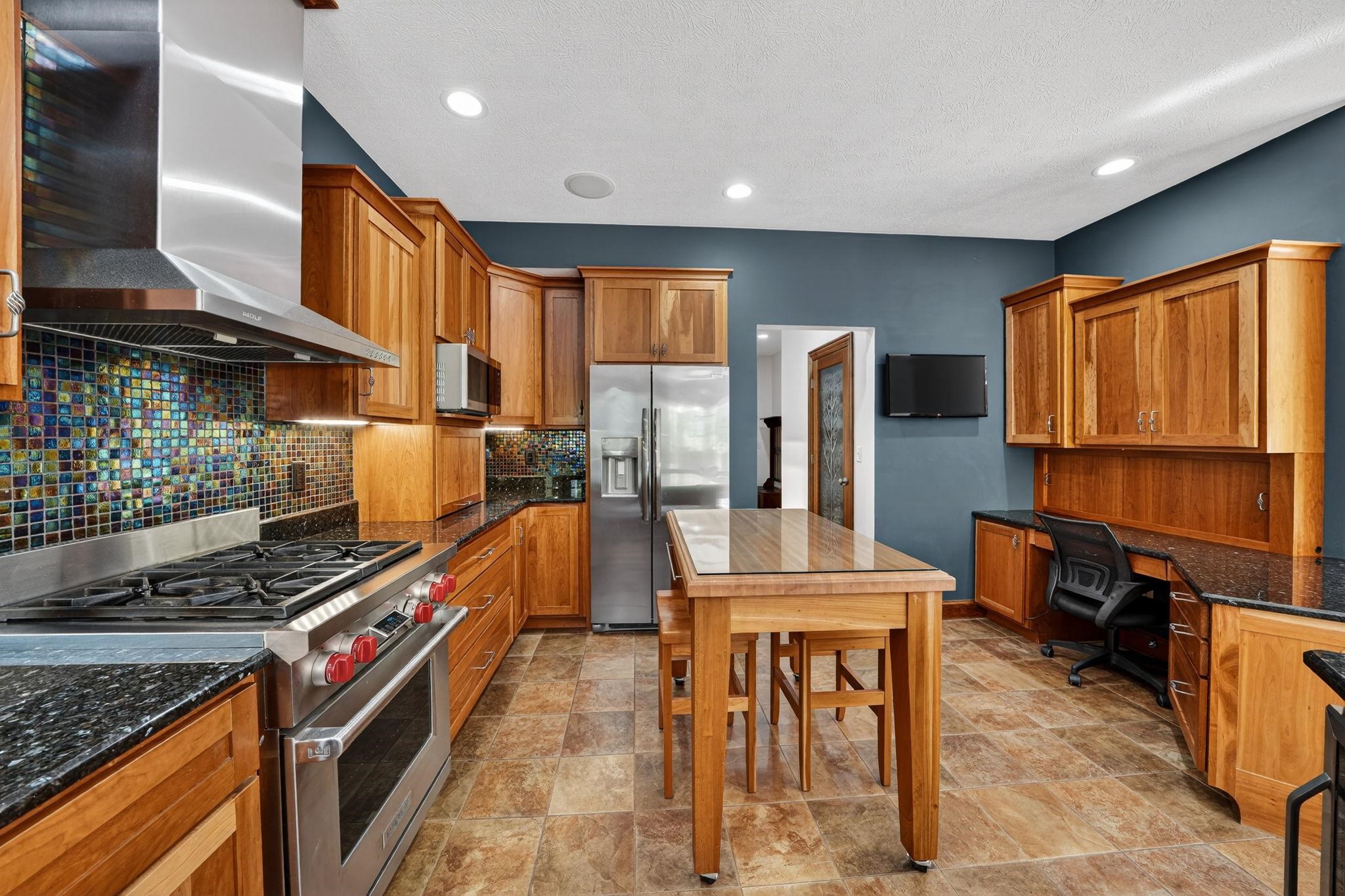 Kitchen featuring wood cabinetry, stainless steel appliances, dark stone countertops, and a mosaic tile backsplash