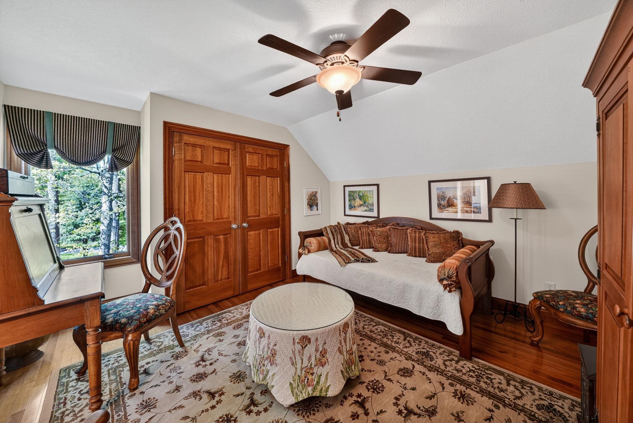 Room featuring a window with exterior tree views, wood-finish flooring, a ceiling fan with integrated lighting, and solid wood double closet doors