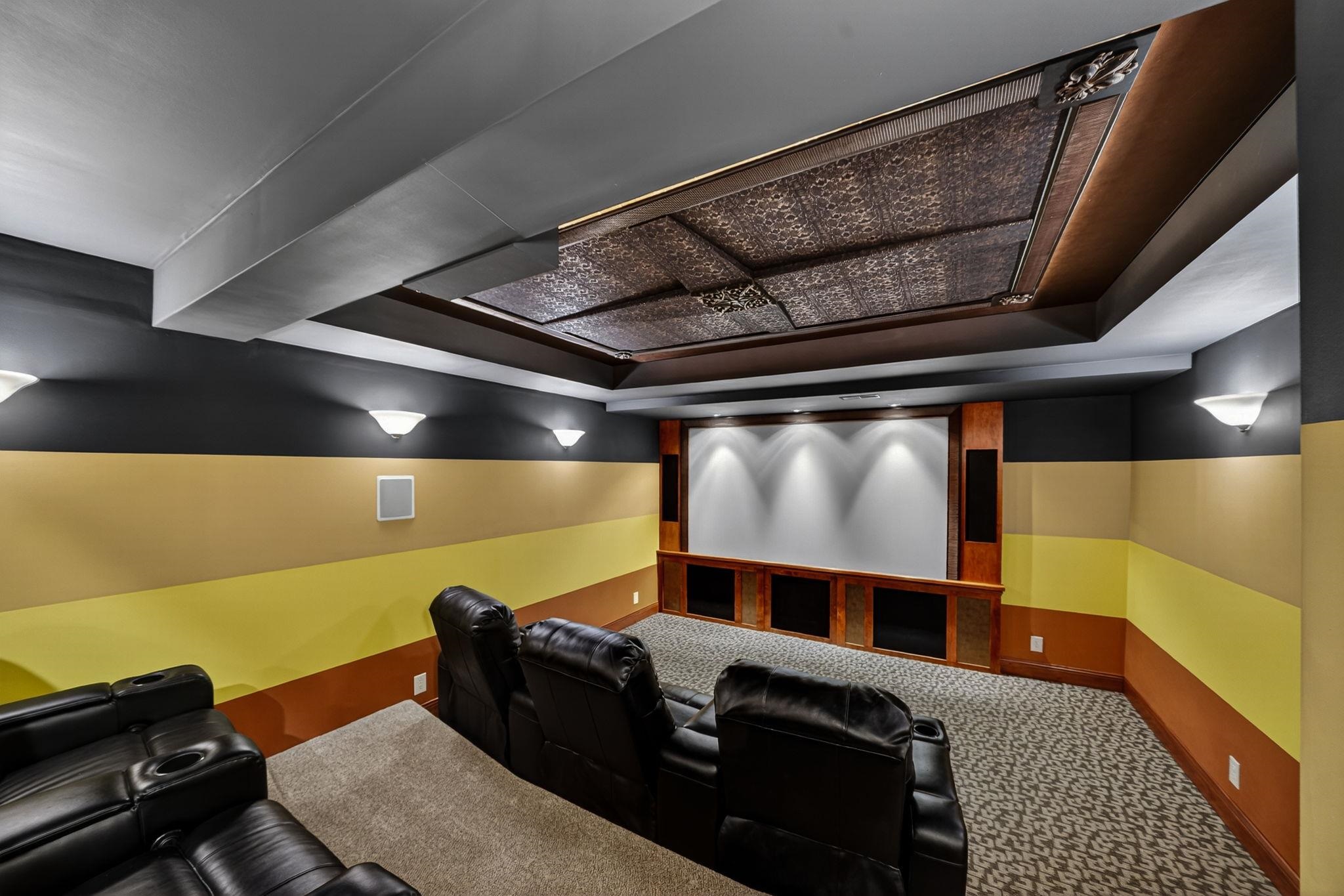 Dedicated home theater featuring a large projection screen, integrated speakers with wood-finish surrounds, and a coffered ceiling with decorative panels