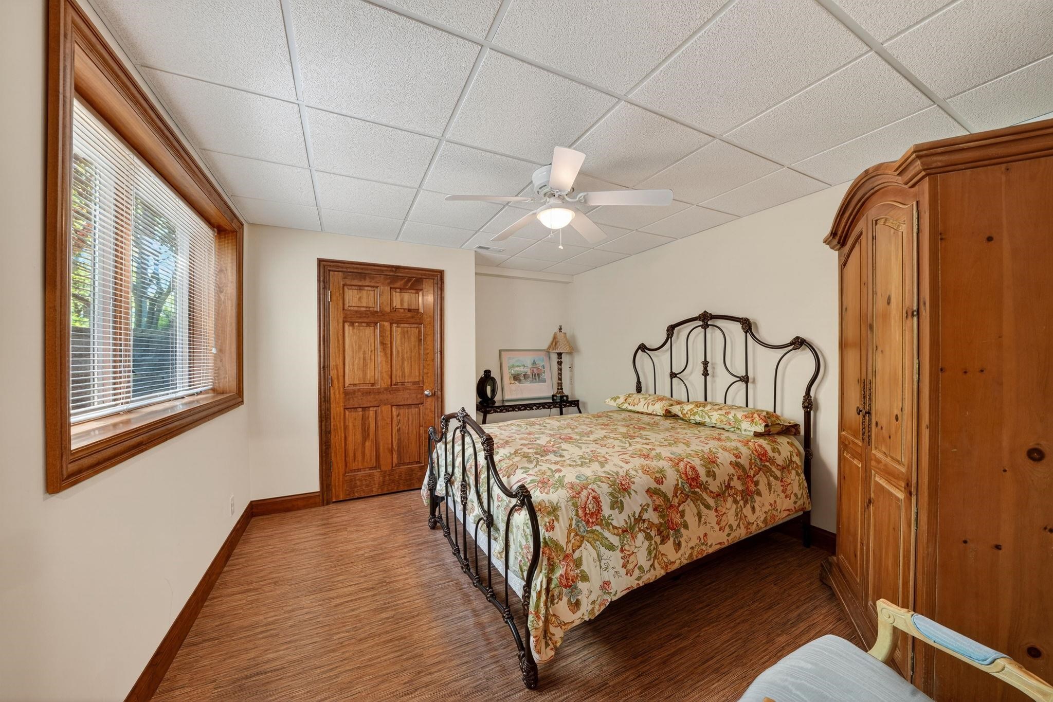 Bedroom featuring wood-finish flooring, a window with wood trim, a paneled wood door, and a ceiling fan with light fixture