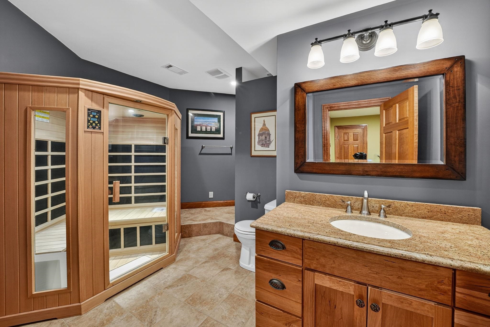 Bathroom featuring a wood-finish vanity with an oval undermount sink, a granite-style countertop, and a framed mirror