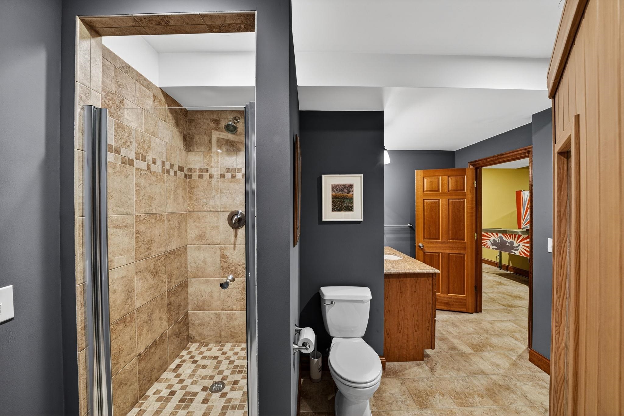 Tiled walk-in shower with glass enclosure, chrome fixtures, and complementary floor tiles