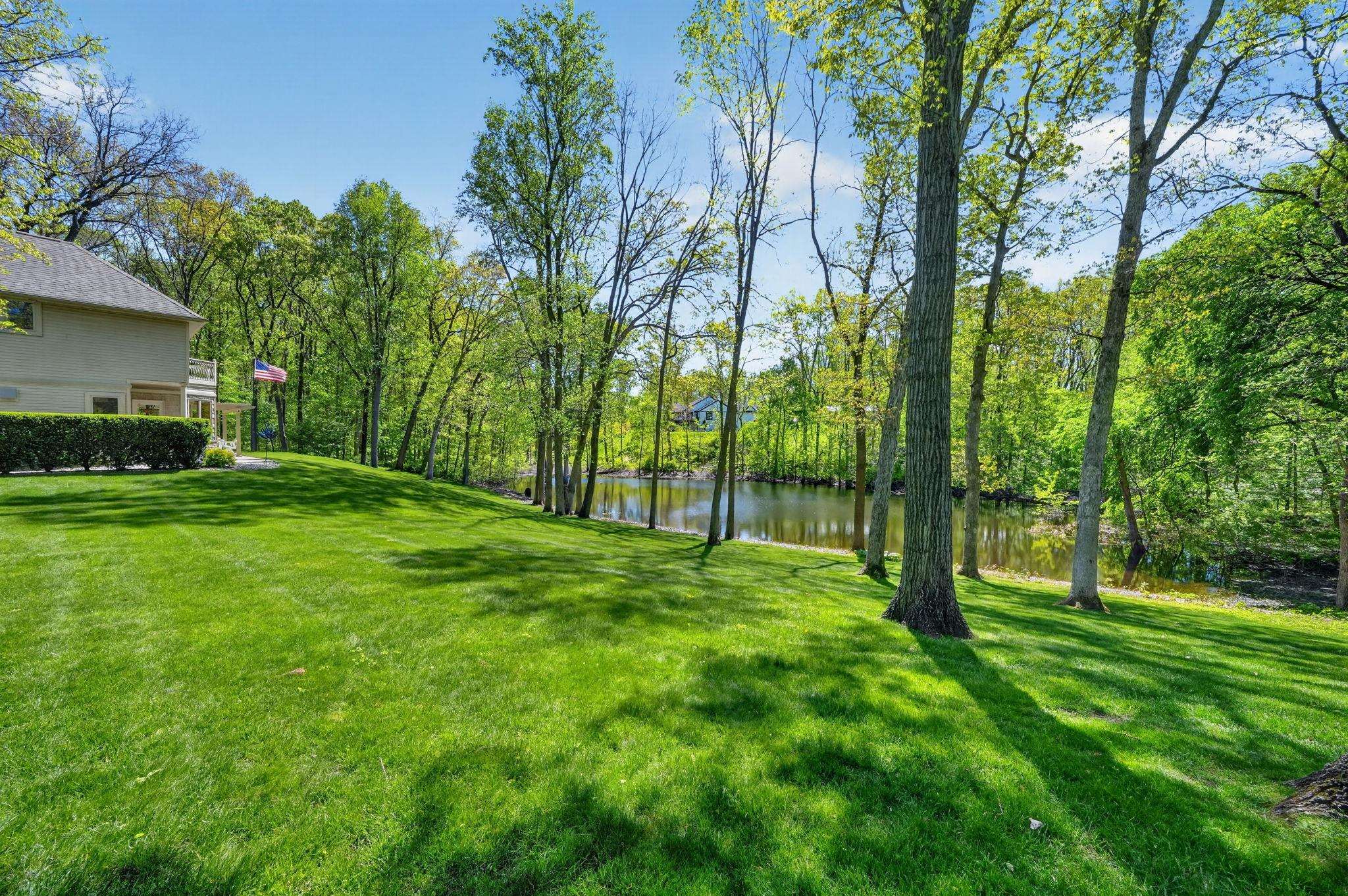 Expansive lawn bordered by mature trees and a tranquil pond