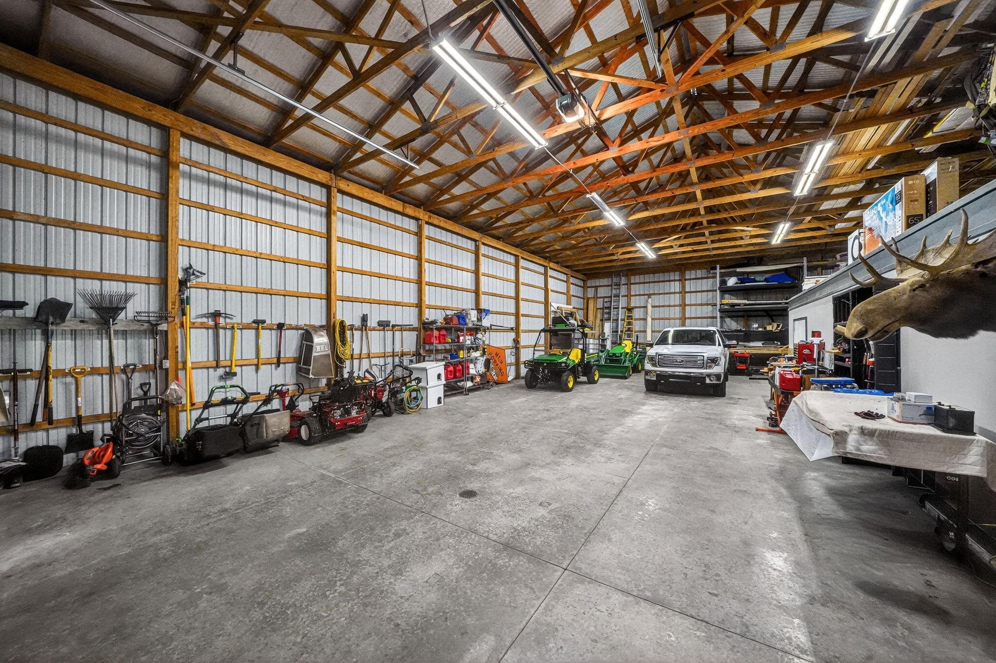 Spacious pole barn with exposed wood beam ceiling, concrete flooring, corrugated metal walls, and overhead fluorescent lighting