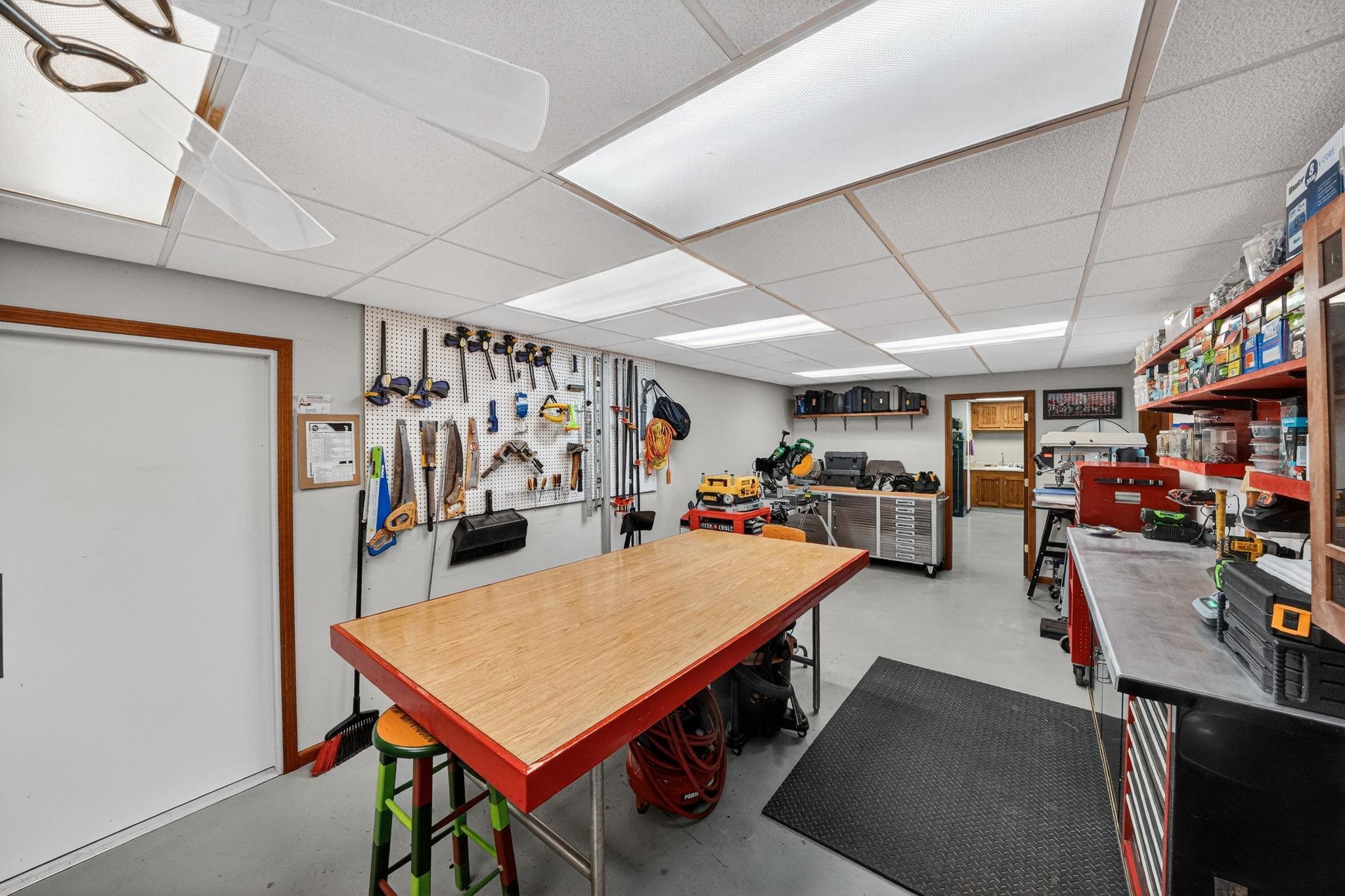 Spacious workshop featuring a large central workbench, extensive pegboard tool storage, built-in shelving, and recessed lighting