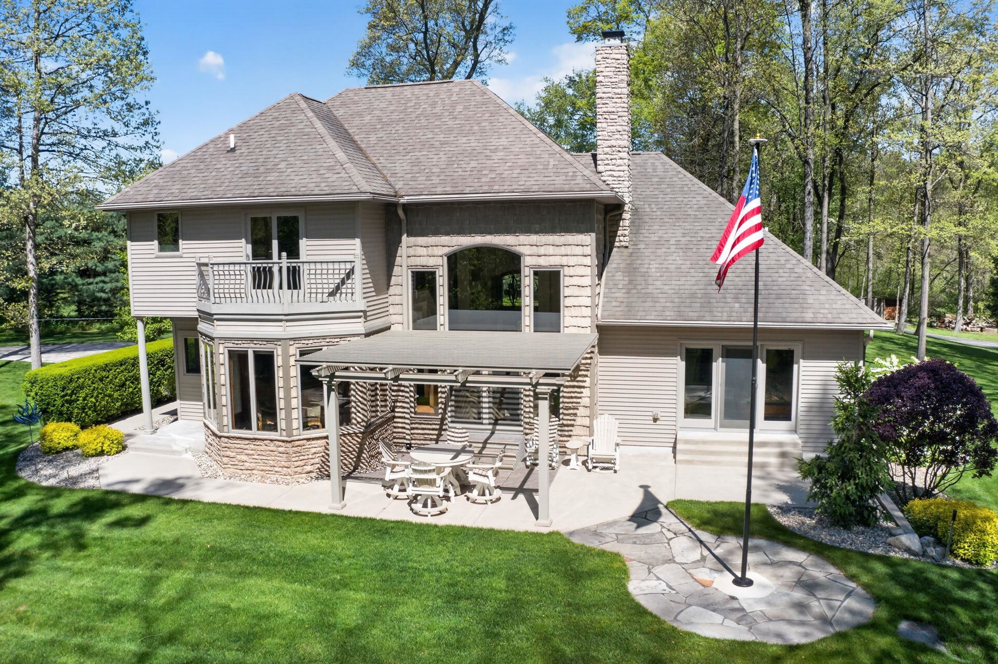 Expansive backyard featuring a manicured lawn, a stone patio with a covered pergola, and mature trees