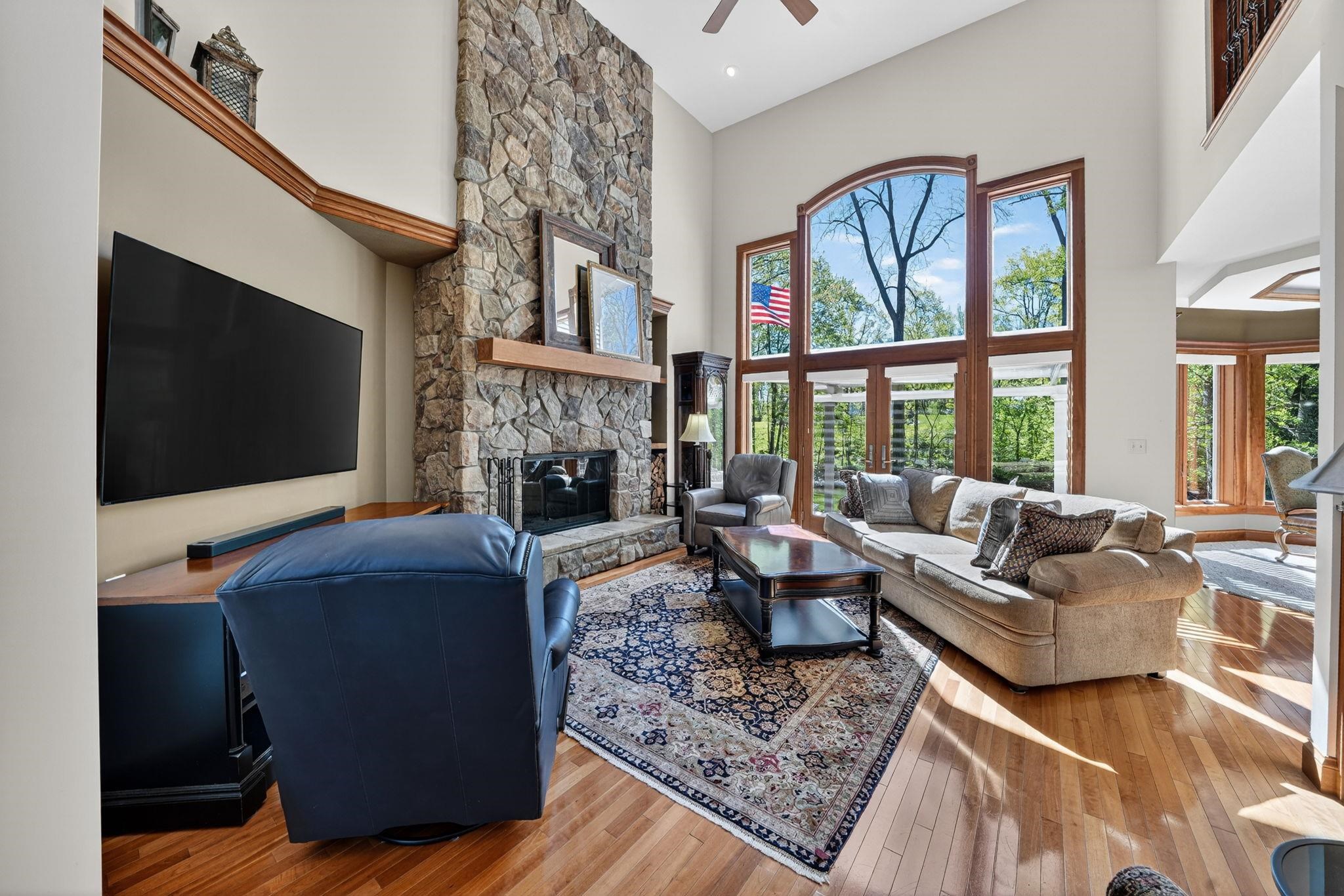 Soaring ceilings with extensive window walls, a floor-to-ceiling stone fireplace, and wood-finish flooring