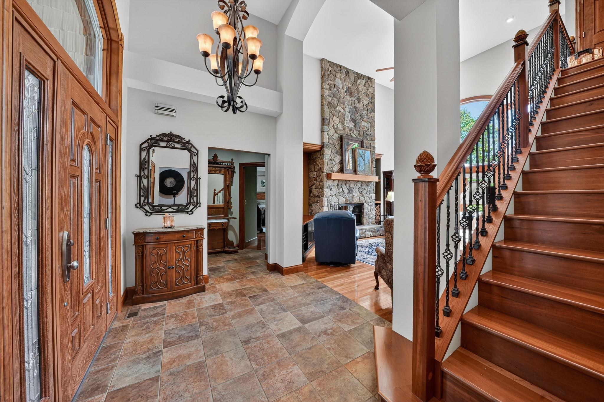 Grand entryway featuring a wood staircase with decorative wrought iron balusters, a stone-faced fireplace, high ceilings, and tile flooring