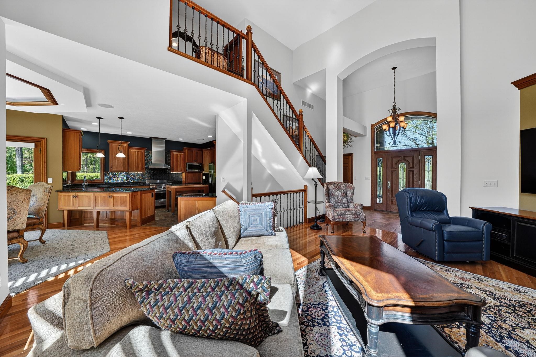Two-story foyer with arched entry and hardwood flooring, featuring a grand staircase with wrought iron balusters, a gourmet kitchen with wood cabinetry and stainless steel appliances, and a living area with high ceilings