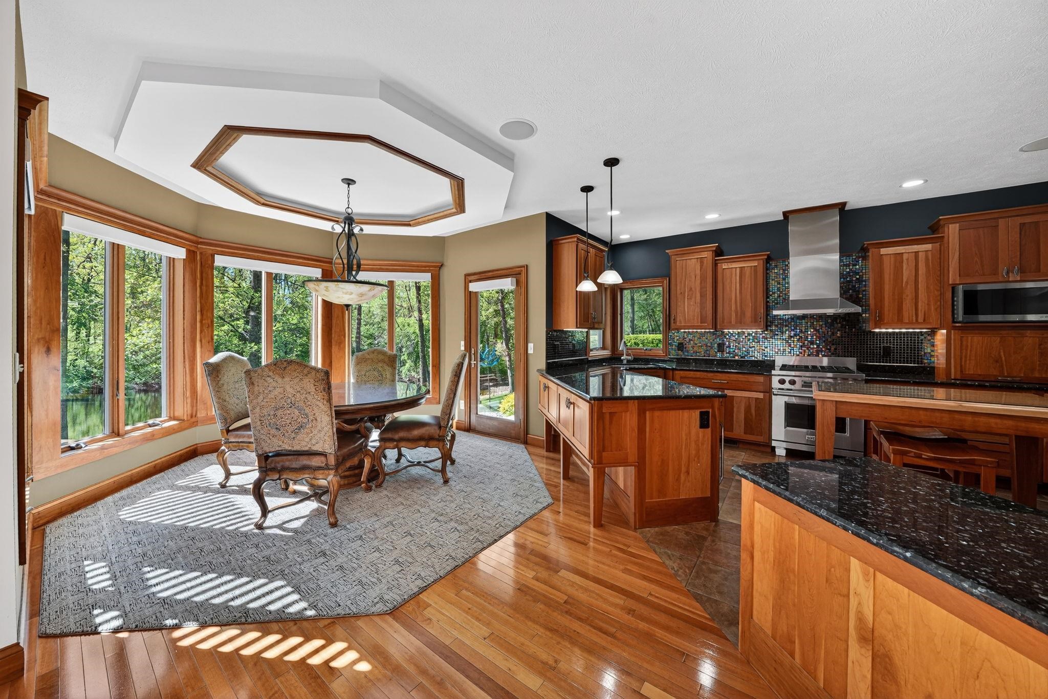 Open-concept kitchen and dining area featuring wood-finish flooring, custom wood cabinetry, dark stone countertops, and a full stainless steel appliance package