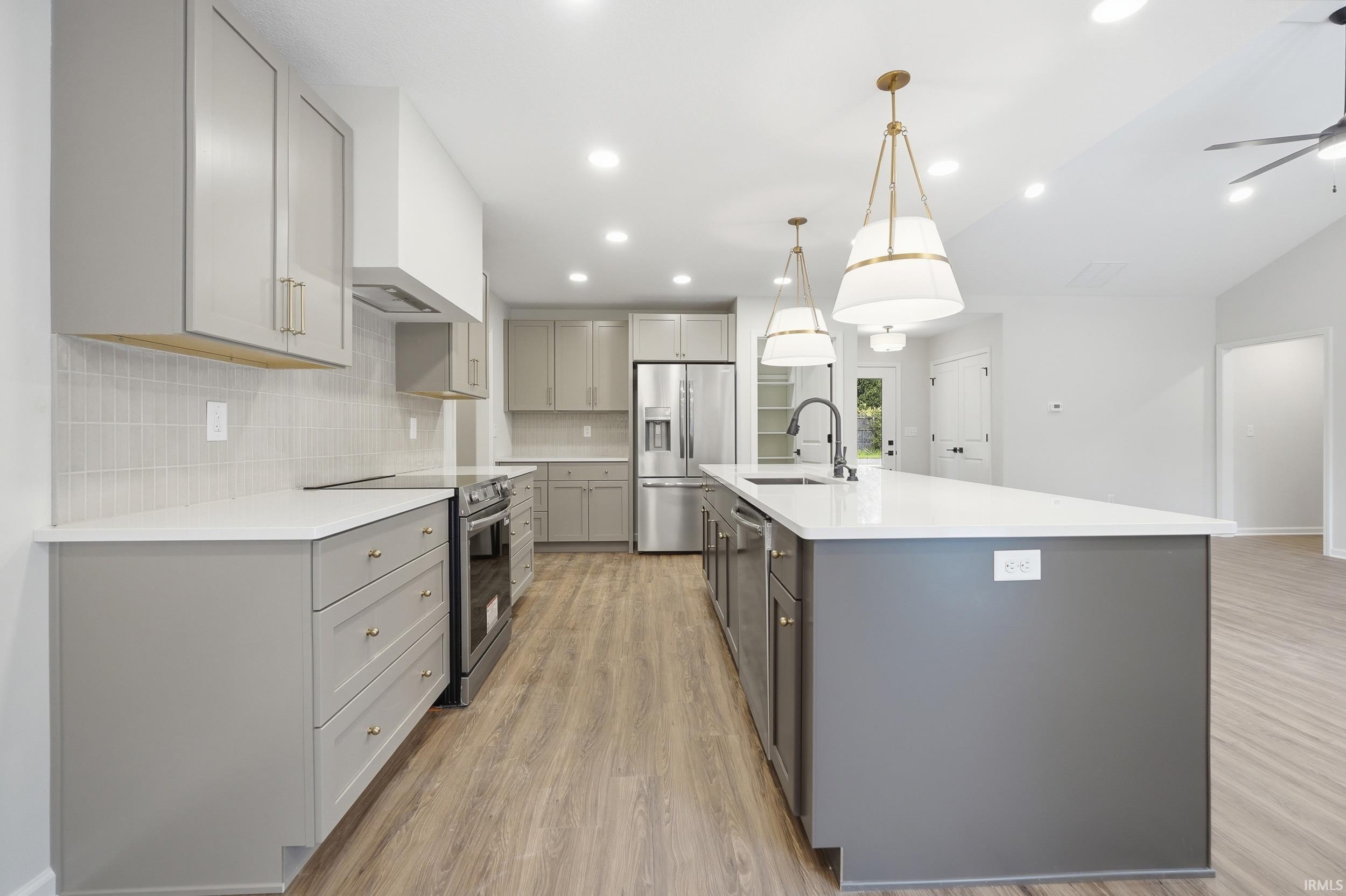 Modern kitchen featuring a large central island, light gray cabinetry, stainless steel appliances, and wood-finish flooring