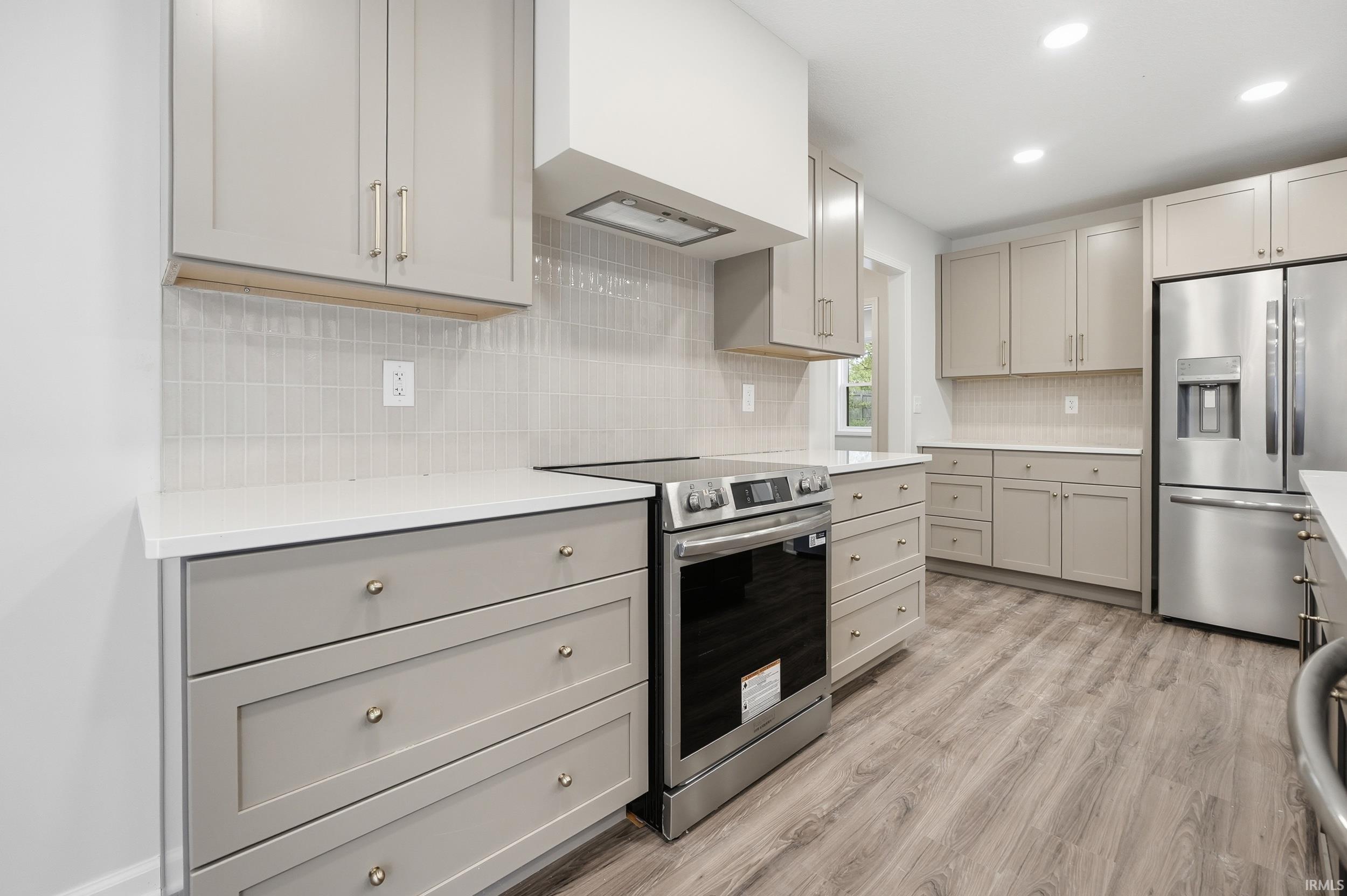 Kitchen featuring light gray shaker cabinetry, stainless steel appliances, solid surface countertops, a white subway tile backsplash, and recessed lighting