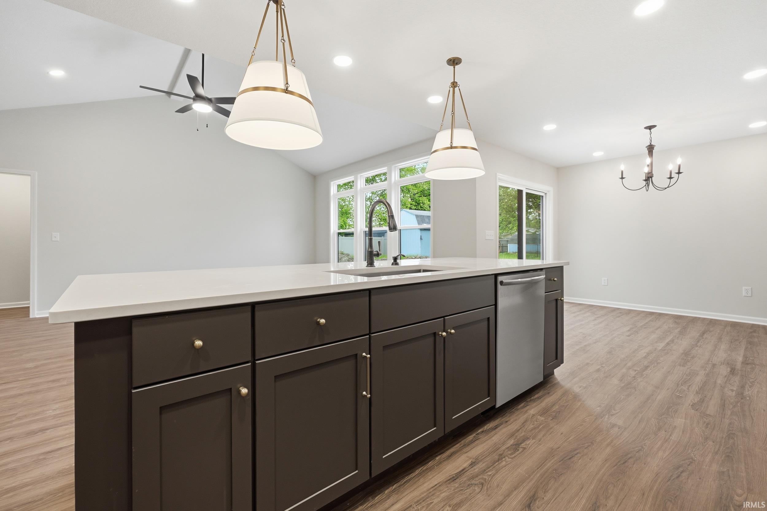 Kitchen island featuring dark cabinetry with brass hardware, a white countertop, and an integrated sink with a matte black faucet