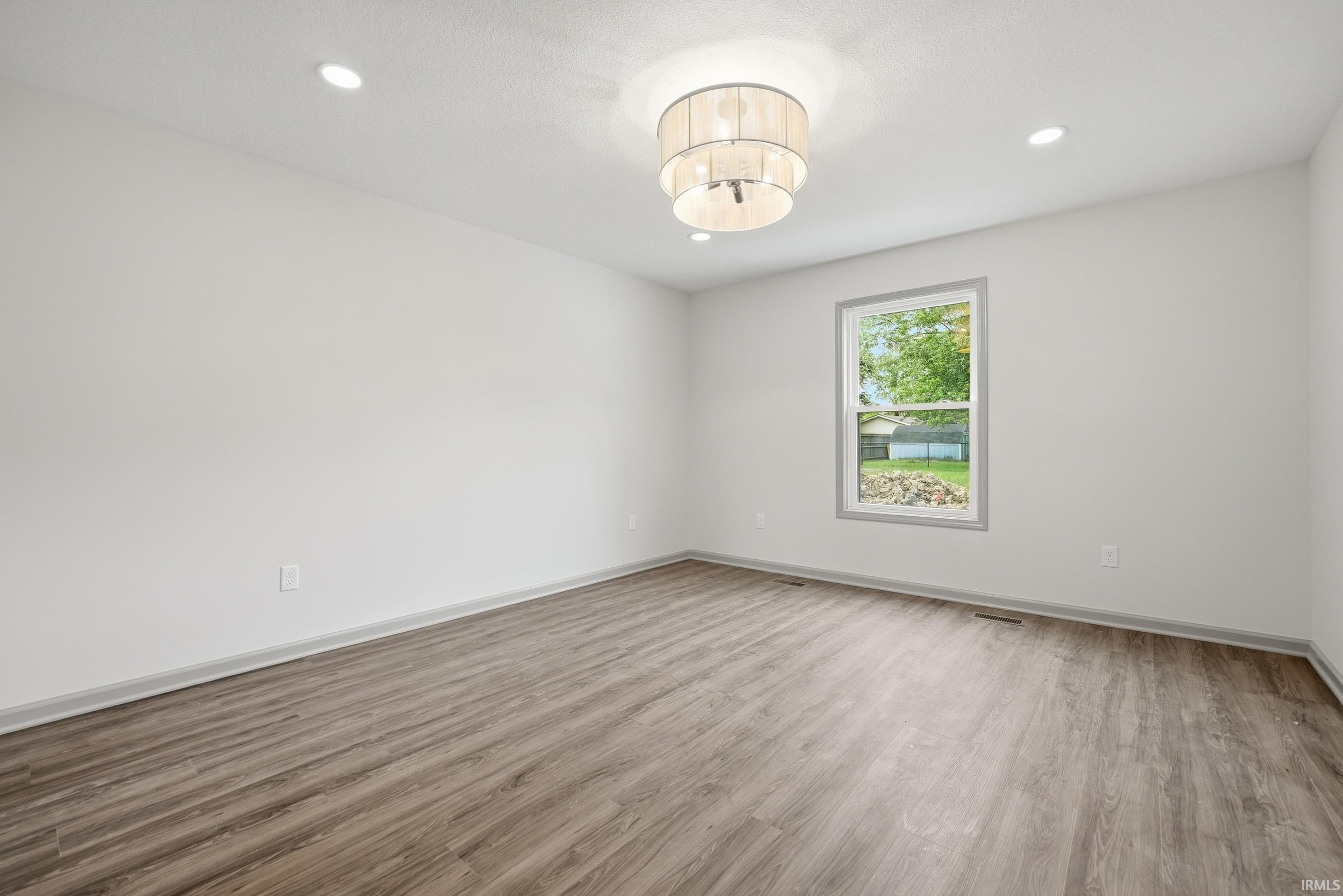 Spacious room featuring wood-finish flooring, white walls, and a contemporary drum pendant light fixture