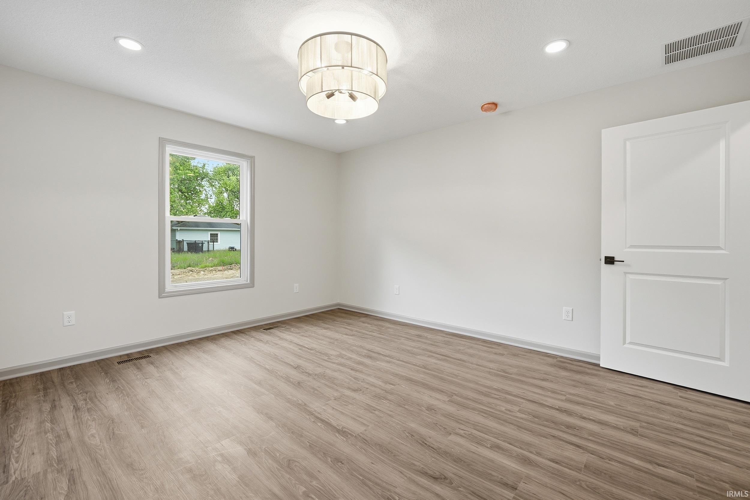 Spacious room featuring wood-finish flooring, light gray walls, a contemporary chandelier, recessed lighting, and a white interior door with black hardware
