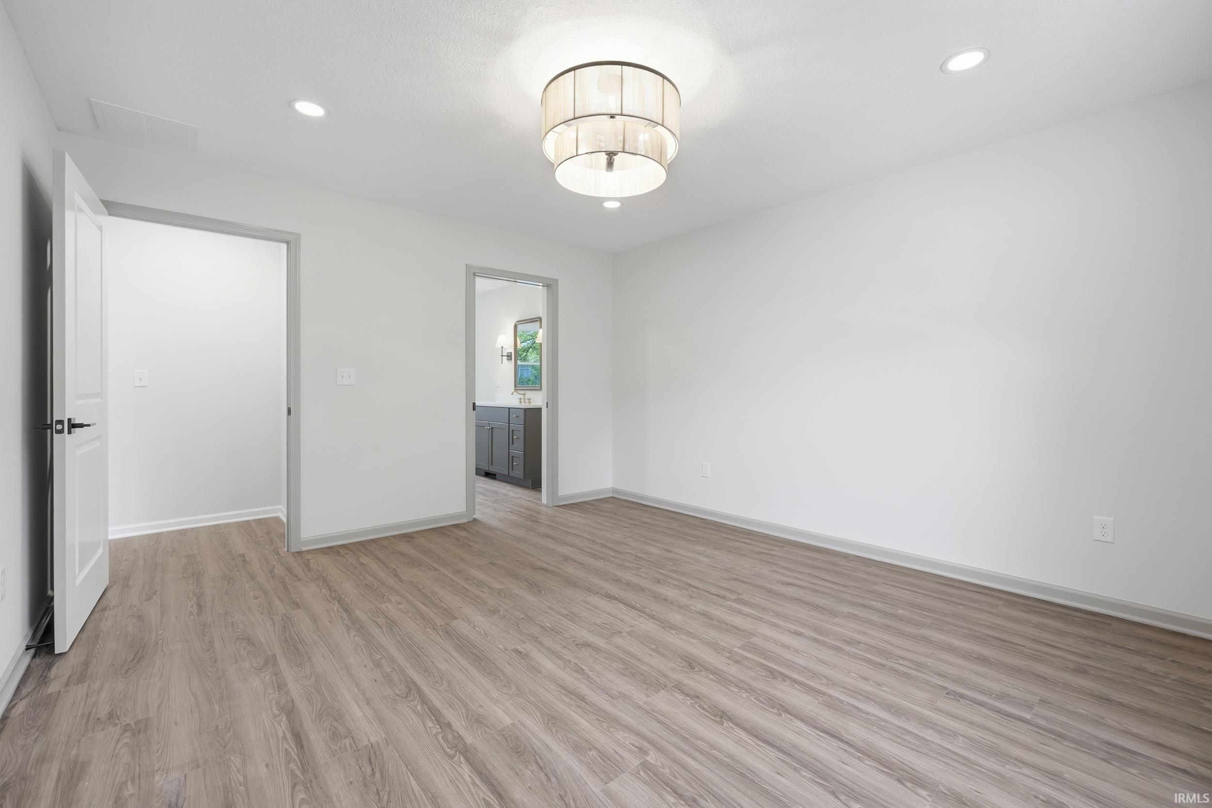 Spacious room featuring wood-finish flooring, white walls, and a contemporary ceiling light fixture