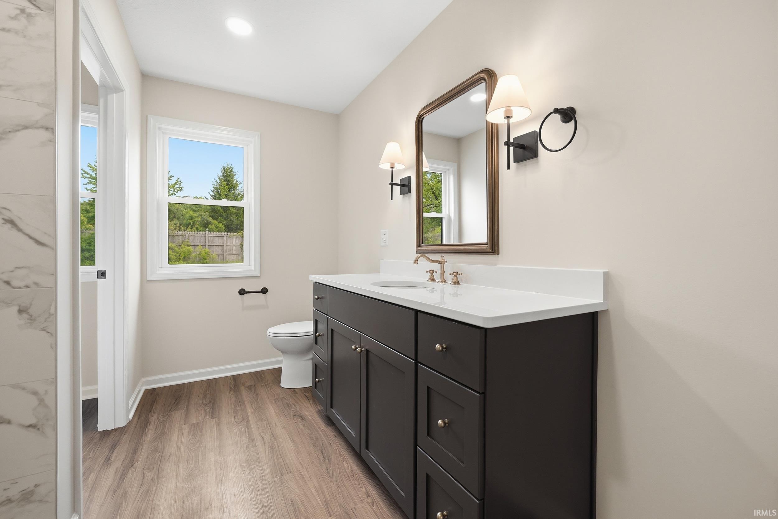 Bathroom featuring a dark wood-finish vanity with a white countertop, an ornate framed mirror, and dual sconces