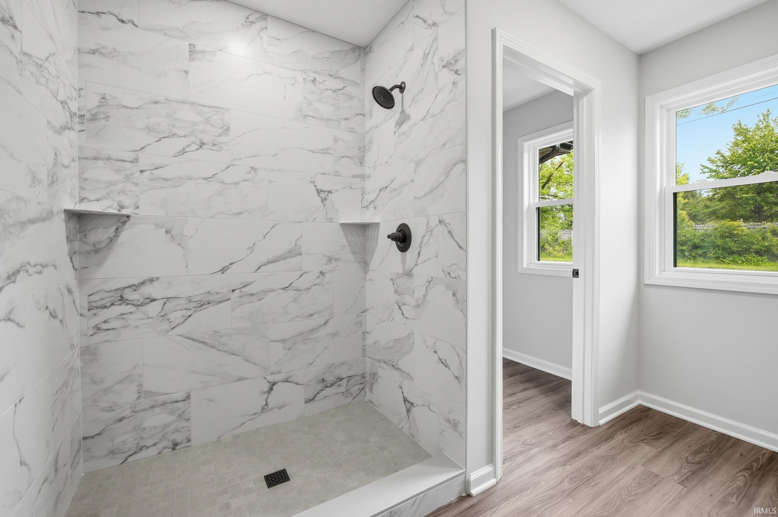 Walk-in shower with large format marble-look tile, integrated shelving, and matte black fixtures
