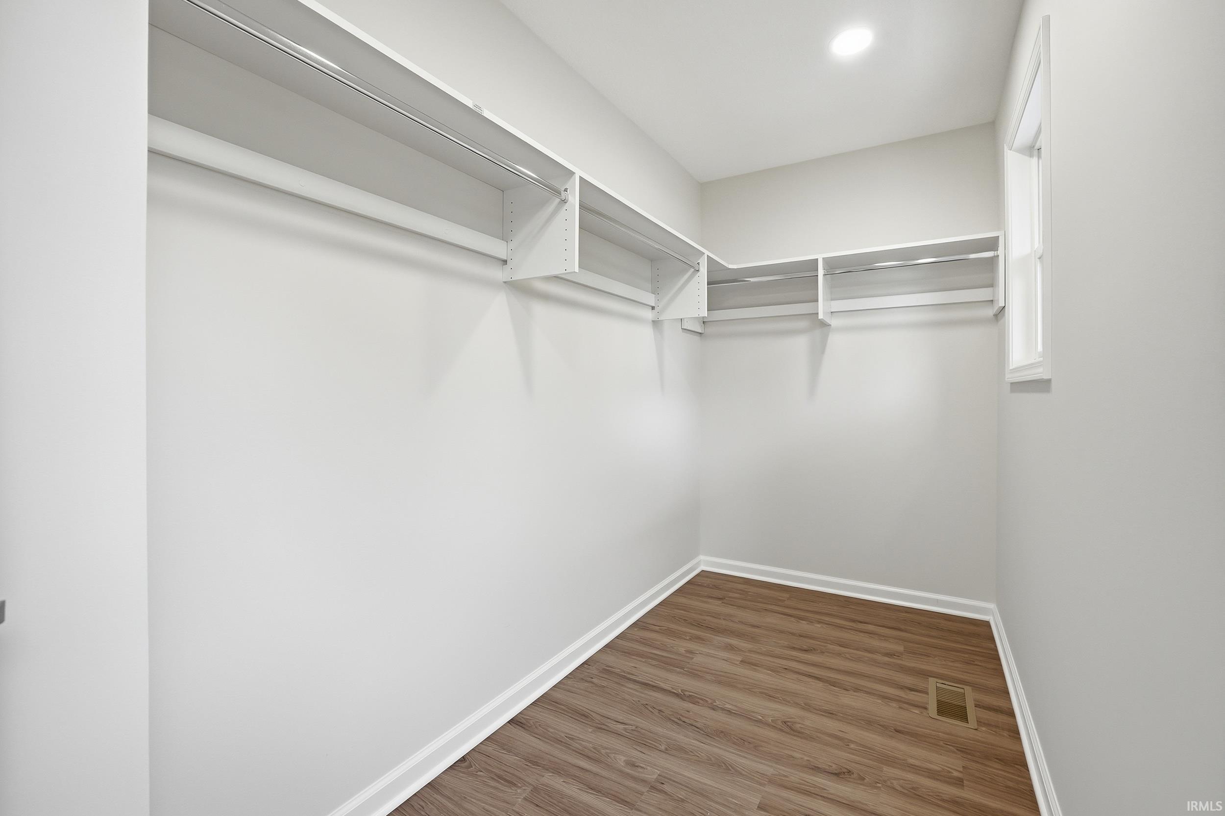 Walk-in closet featuring extensive built-in shelving, multiple hanging rods, wood-finish flooring, and natural light from a window