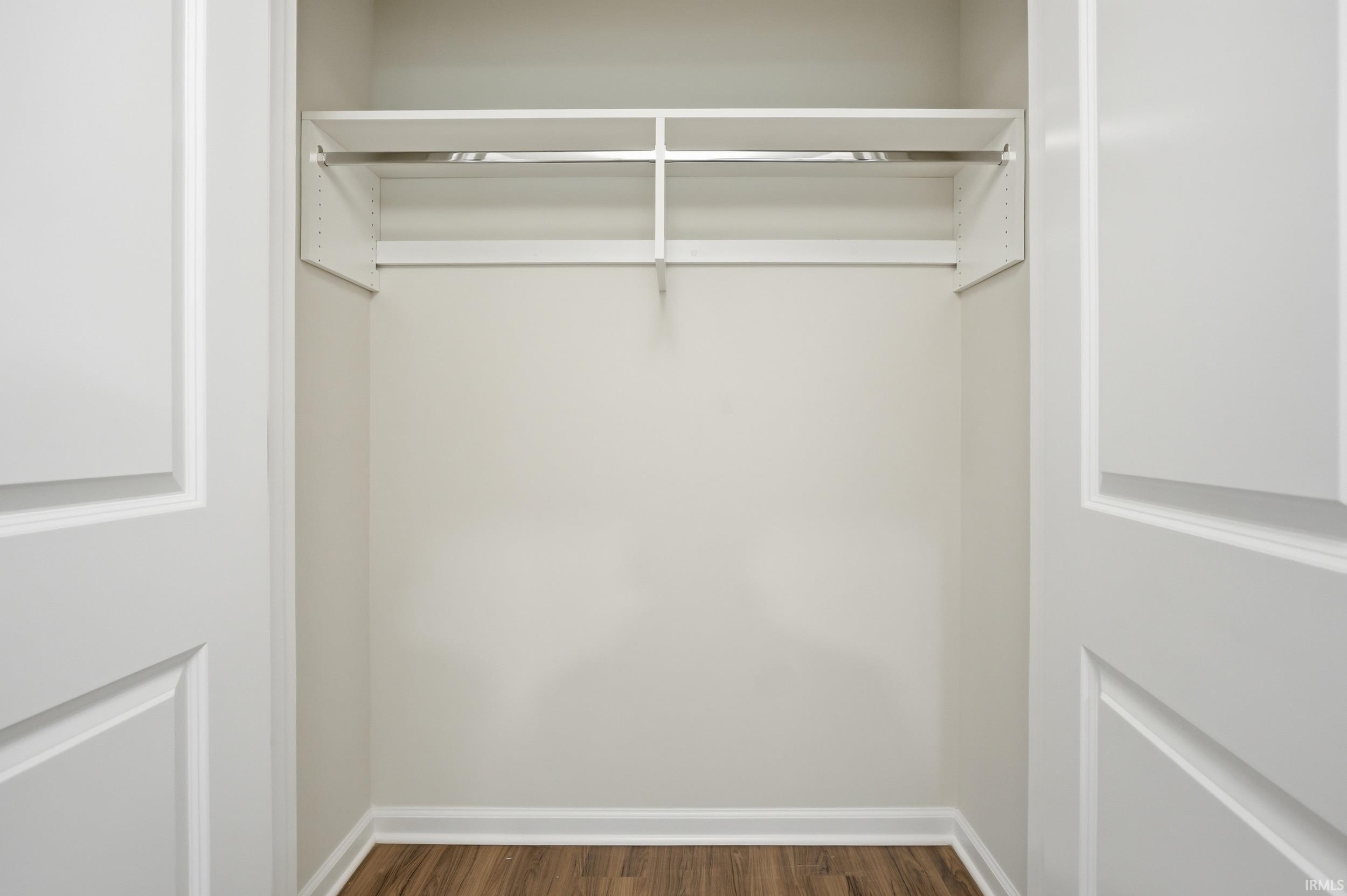 Open closet featuring white shelving and chrome hanging rods