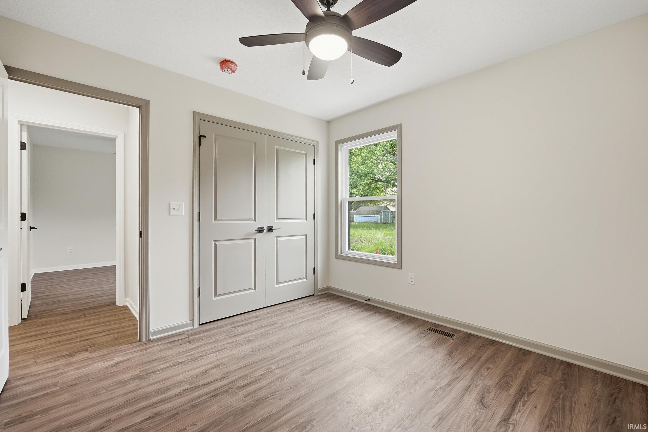 Interior room featuring durable wood-finish flooring, light-toned walls, and a ceiling fan with integrated lighting