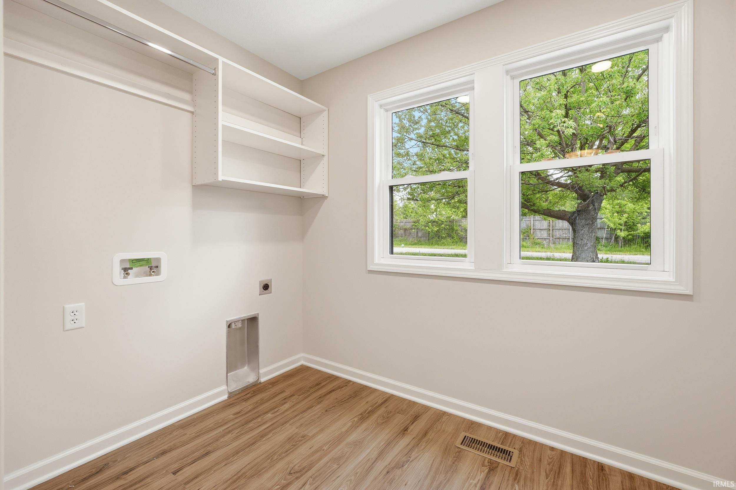 Utility room featuring wood-finish flooring, two large windows, white trim, built-in shelving, and a hanging clothes rod