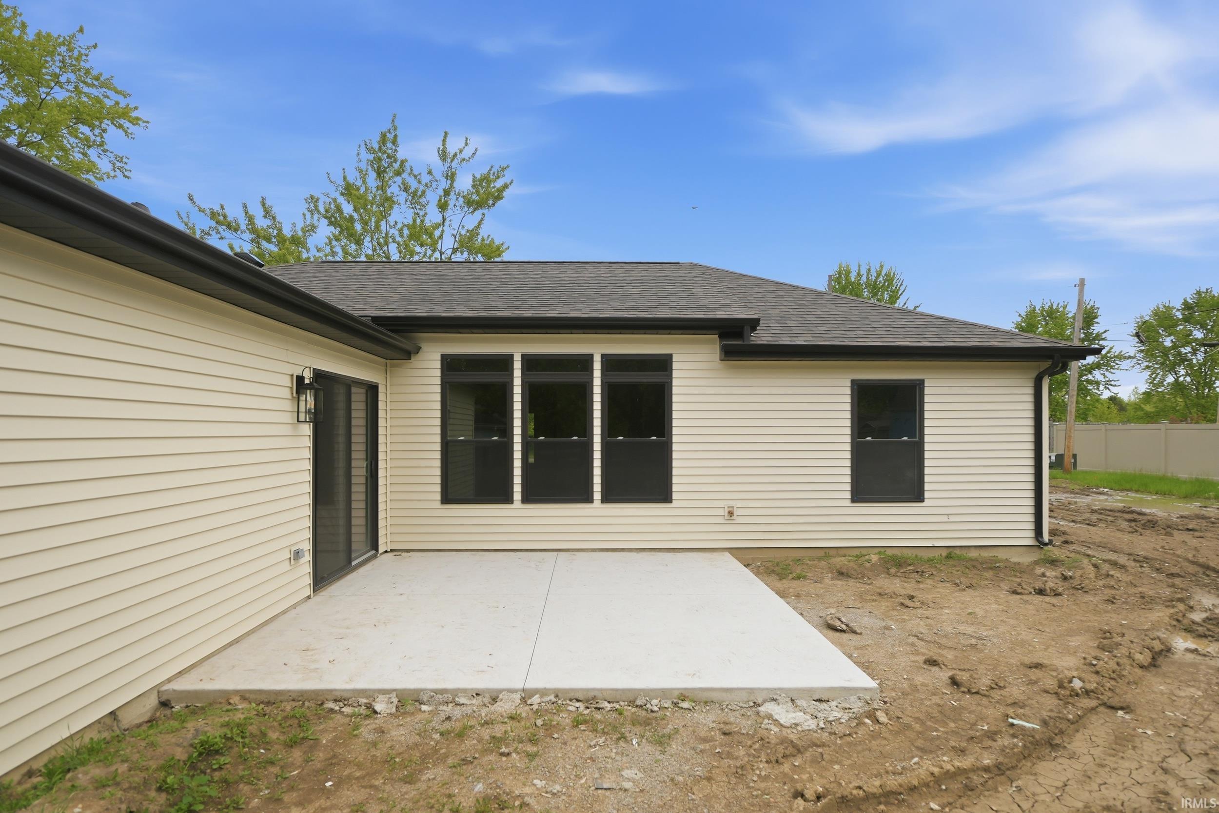 Rear exterior featuring a concrete patio, light-colored horizontal siding, dark window frames, and a dark shingle roof
