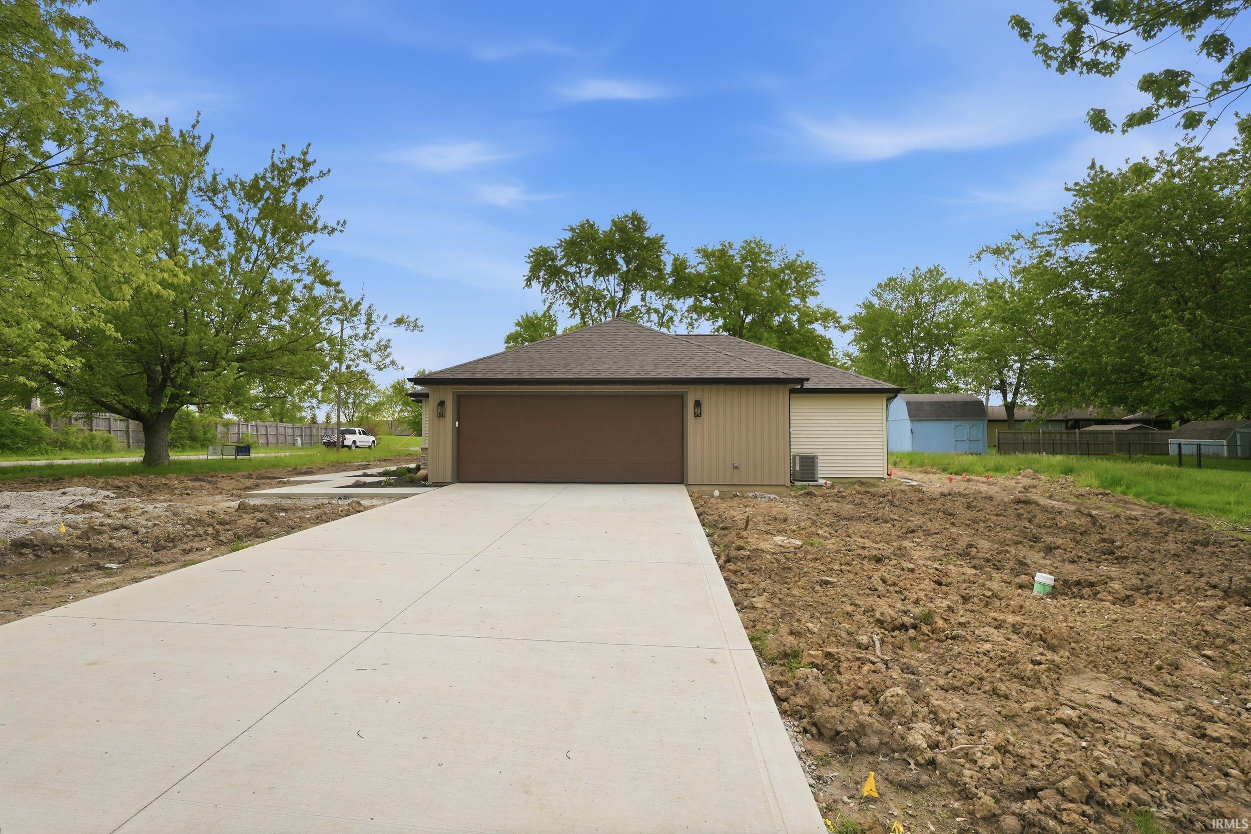 Newly constructed residence featuring a neutral siding exterior, an attached garage with a brown door, a paved driveway, and a dark shingle roof