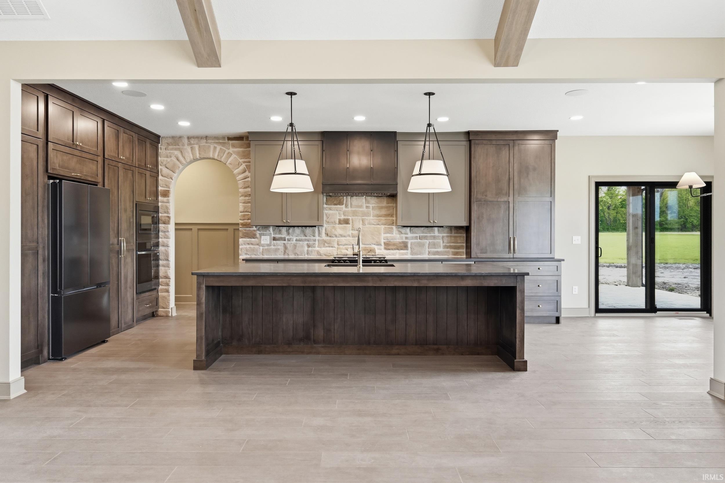 Open-concept kitchen featuring a large central island with dark wood cabinetry, integrated appliances, a stone tile backsplash, and two hanging pendant lights