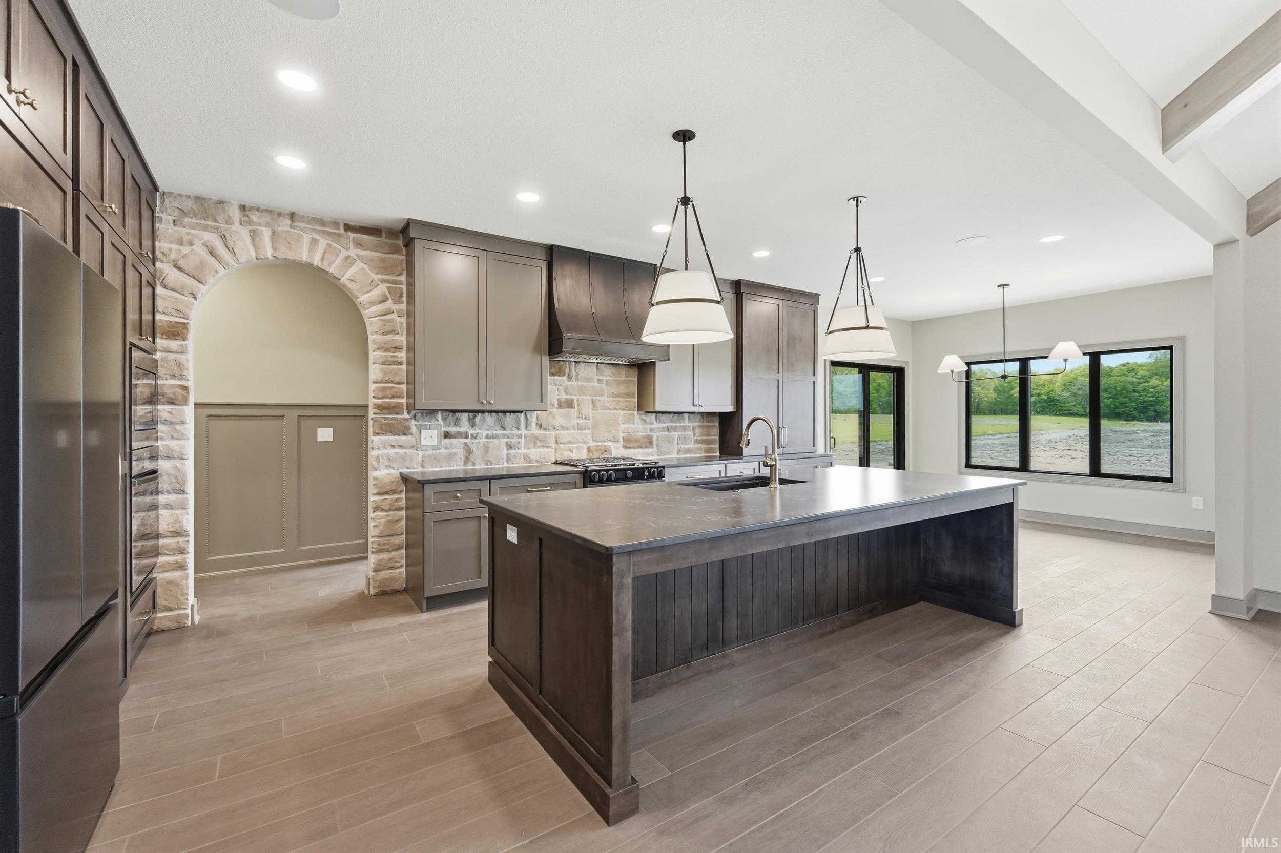 Modern kitchen featuring a large center island with integrated sink, stainless steel appliances, pendant lighting, and recessed ceiling lights