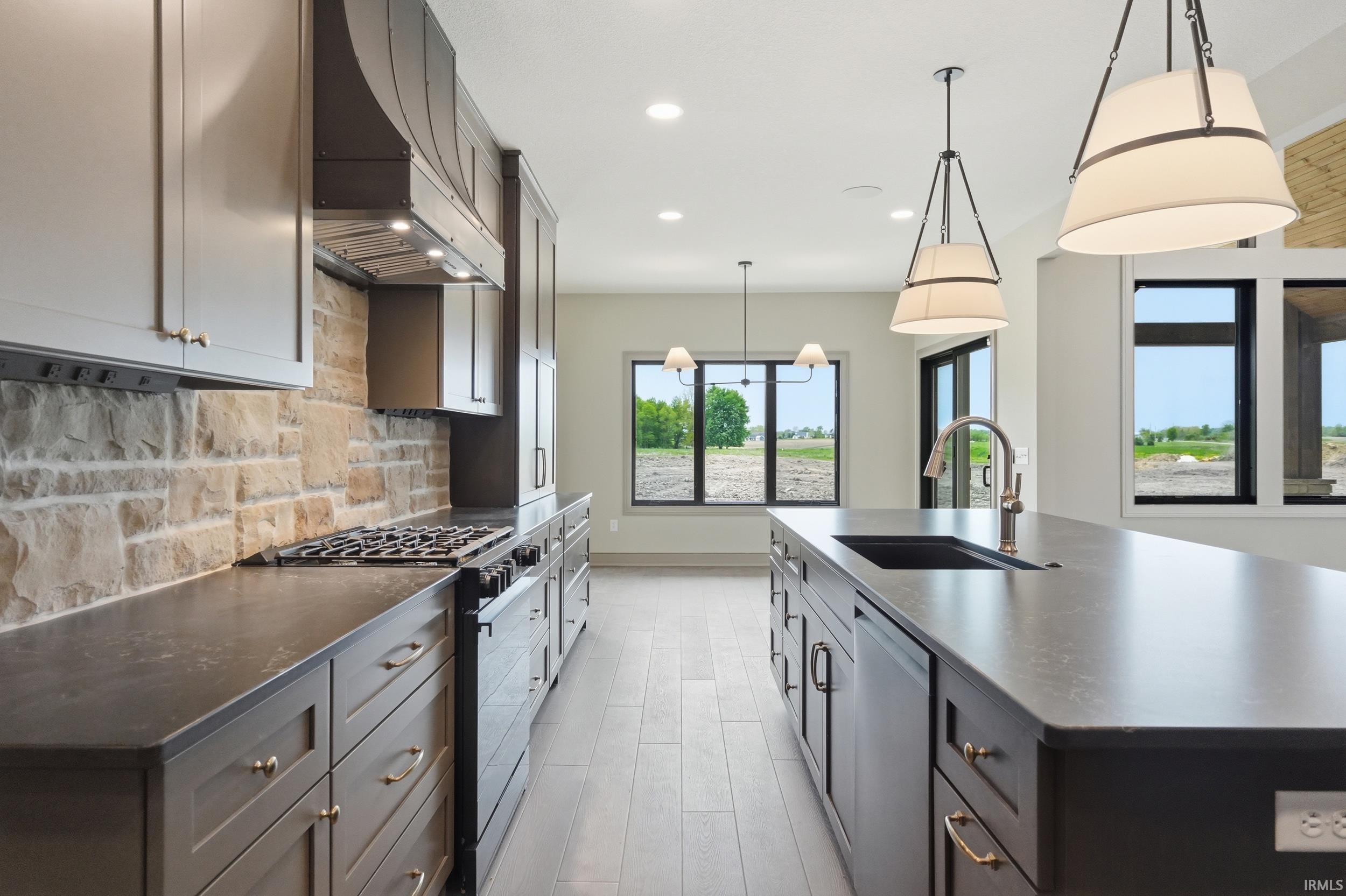 Gourmet kitchen featuring a substantial island, built-in stainless steel appliances, stone backsplash, rich cabinetry, and pendant lighting