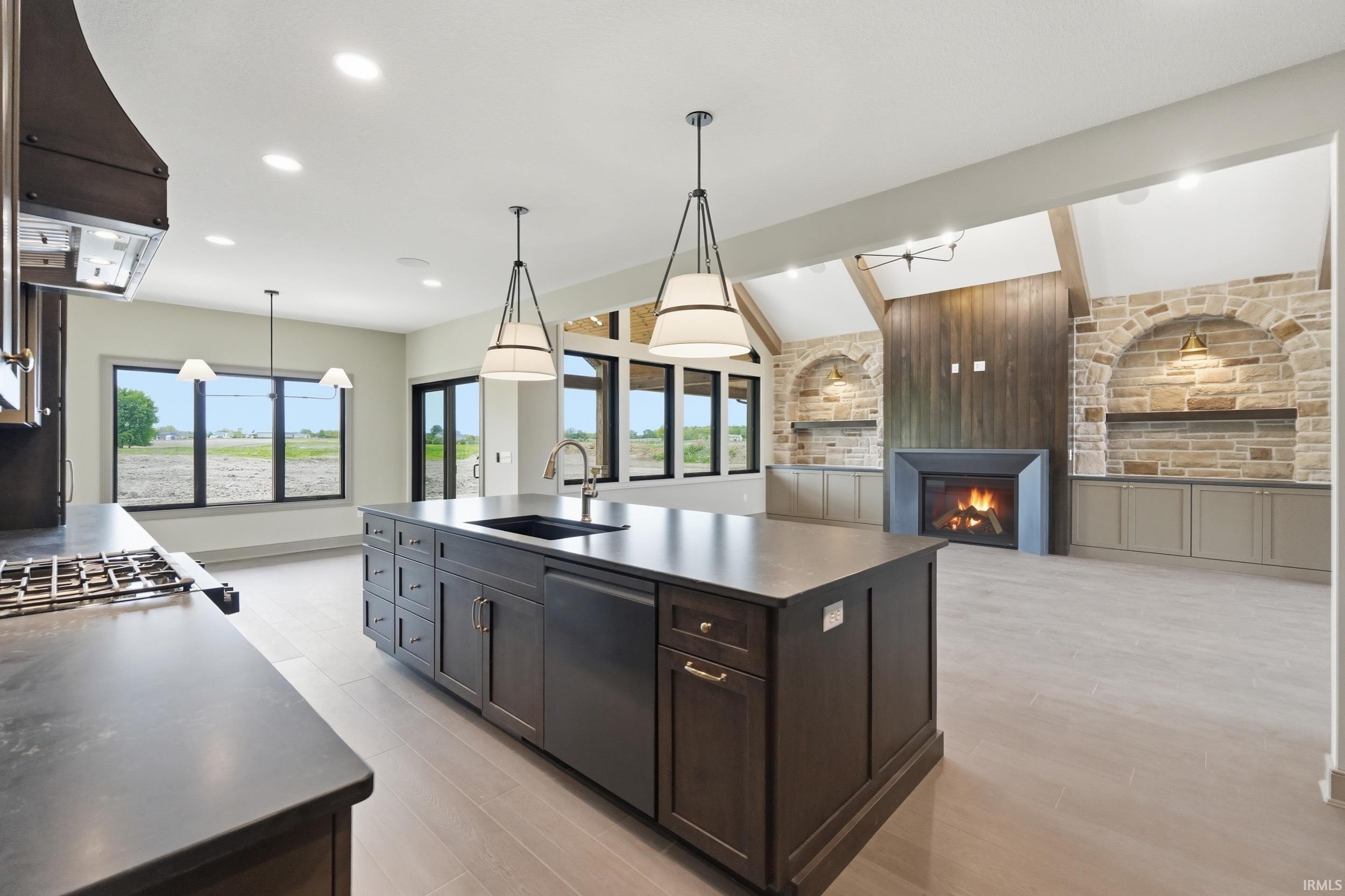 Kitchen island with integrated sink and dishwasher, pendant lighting, gas range with range hood, and light wood-finish flooring