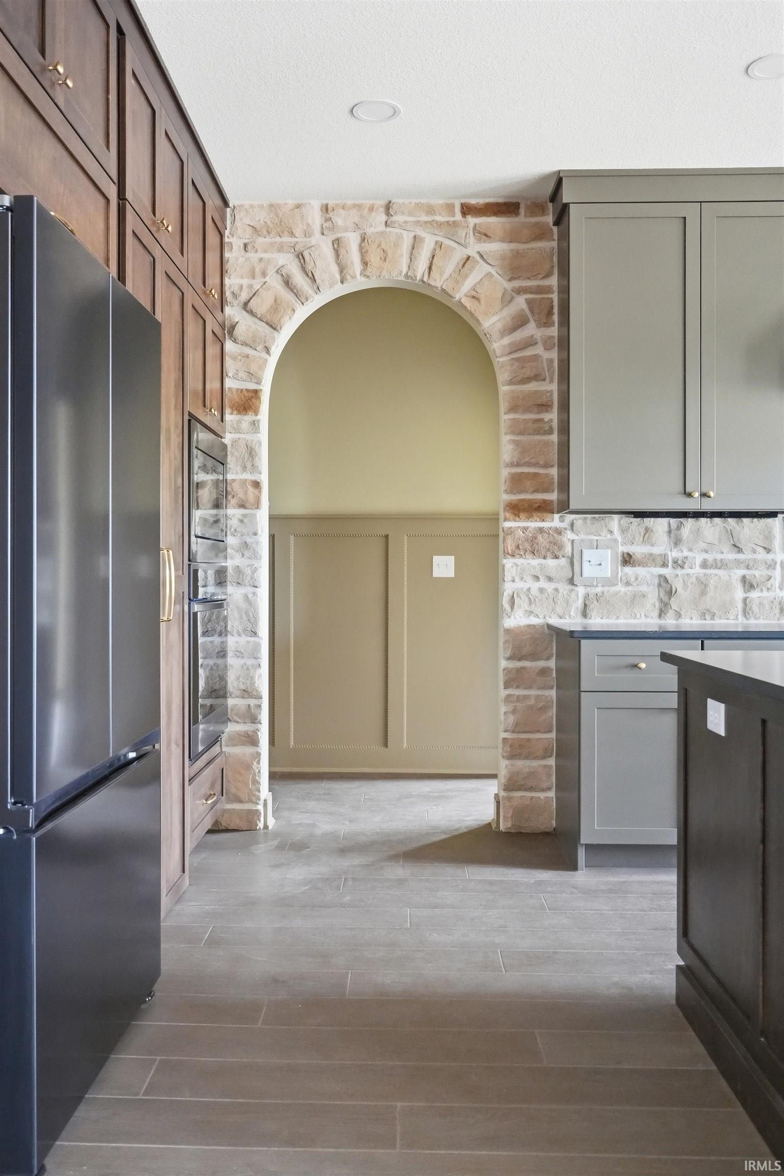 Kitchen featuring an arched stone entry, dark wood-finish flooring, recessed lighting, and built-in cabinetry with a modern refrigerator