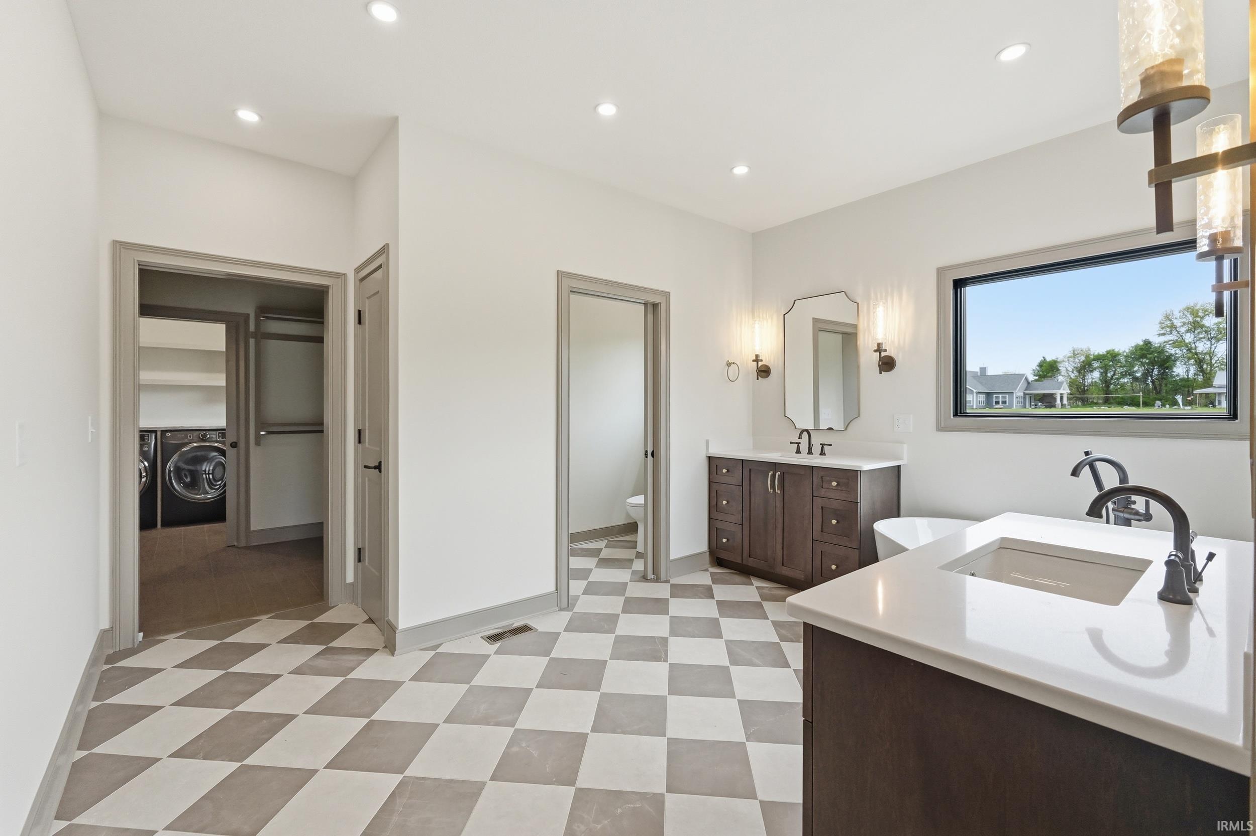 Spacious bathroom featuring checkered tile flooring, a large window, and dual vanities with integrated sinks