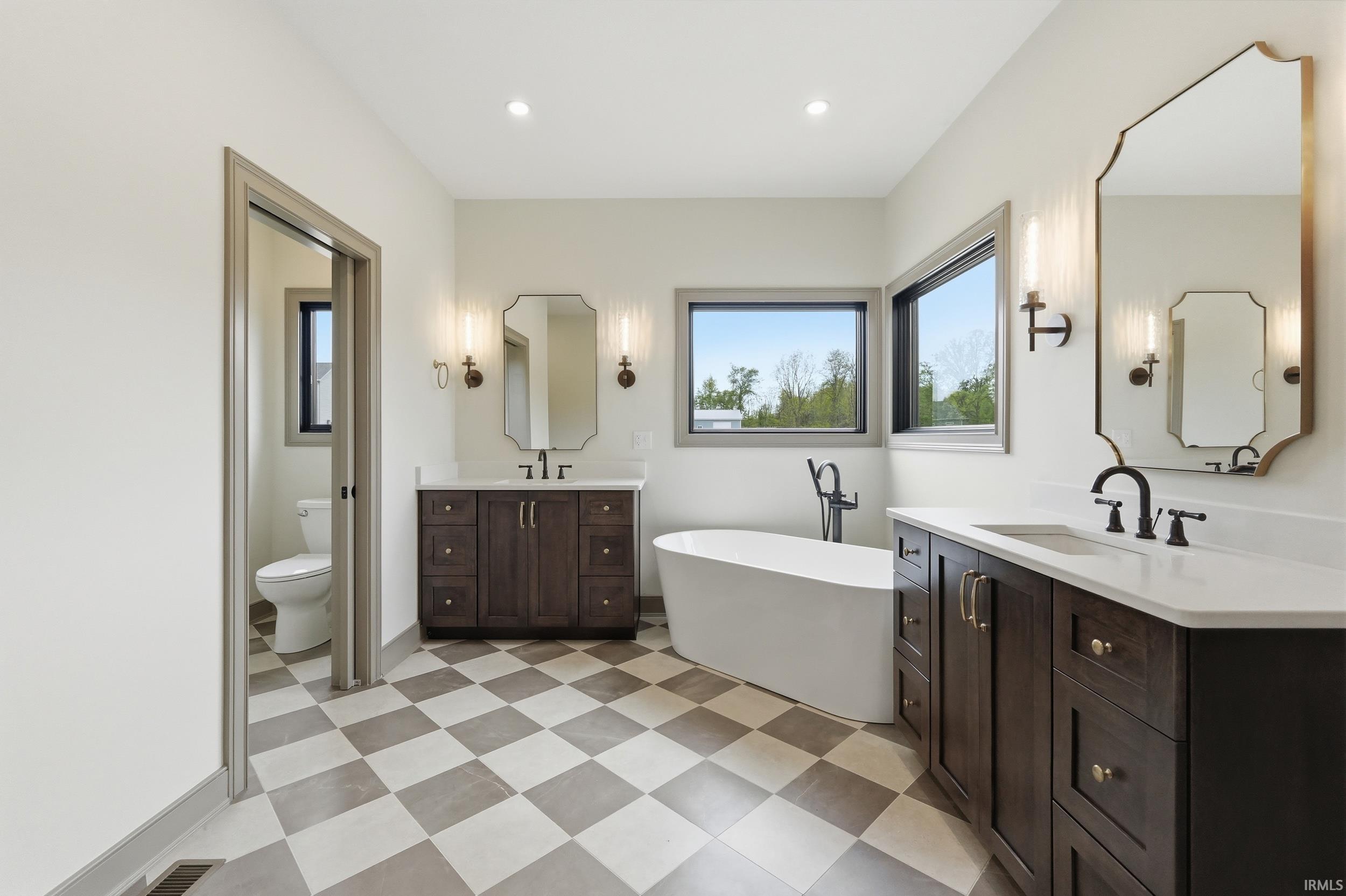Bathroom featuring a freestanding soaking tub, dual dark wood-finish vanities with light countertops, and a checkered floor